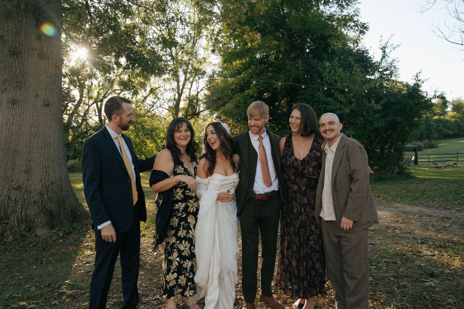 A group gathers outdoors for a wedding photo by a large tree at sunset.