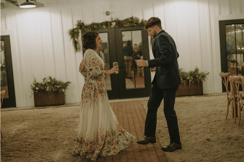 A couple dances together in a rustic indoor venue with floral decorations.