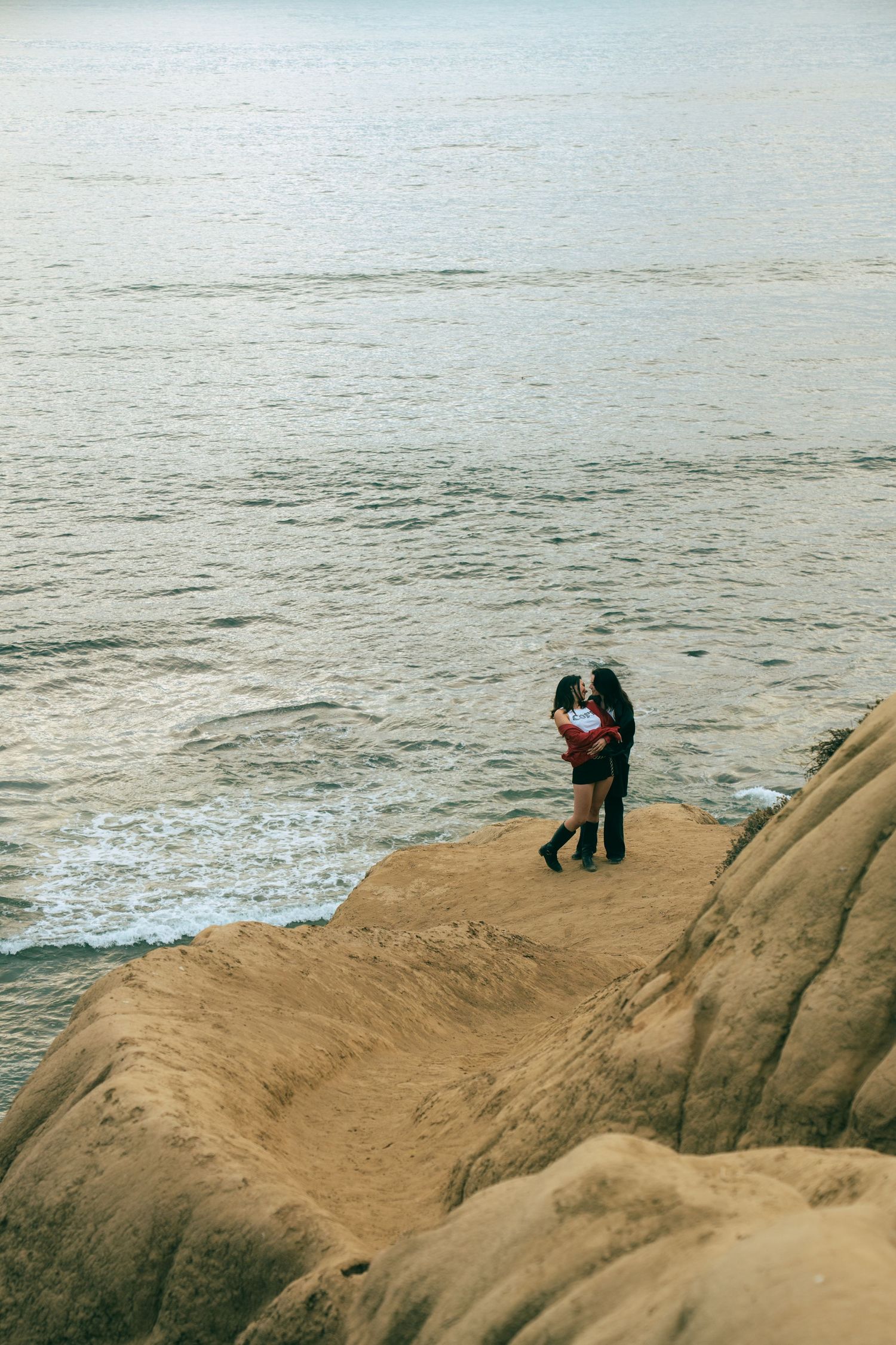 Couple sitting together on coastal cliffs overlooking misty ocean views in sequence of progressive shots.