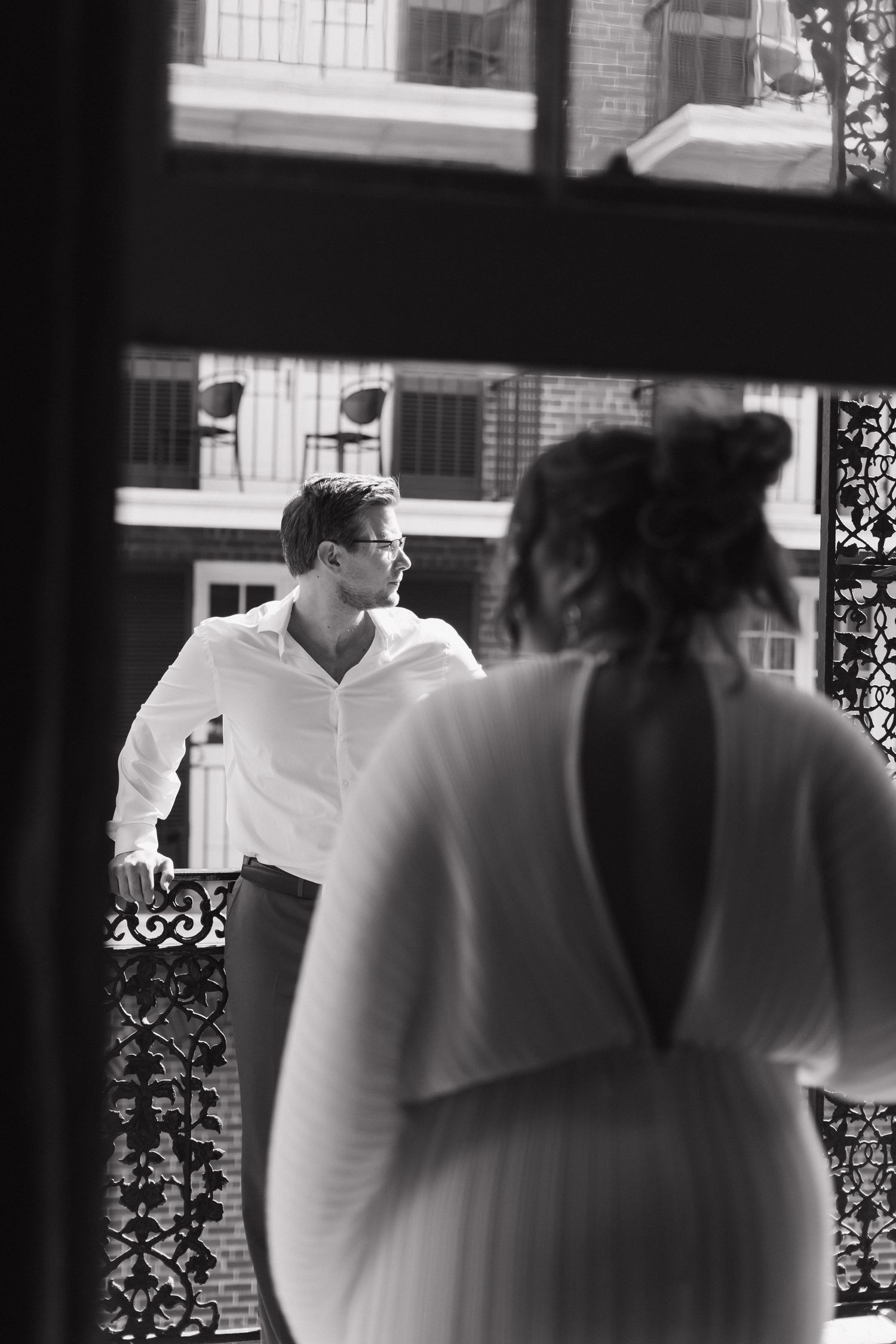 Black and white photo of couple sharing intimate moment on balcony with brick building backdrop. New Orleans