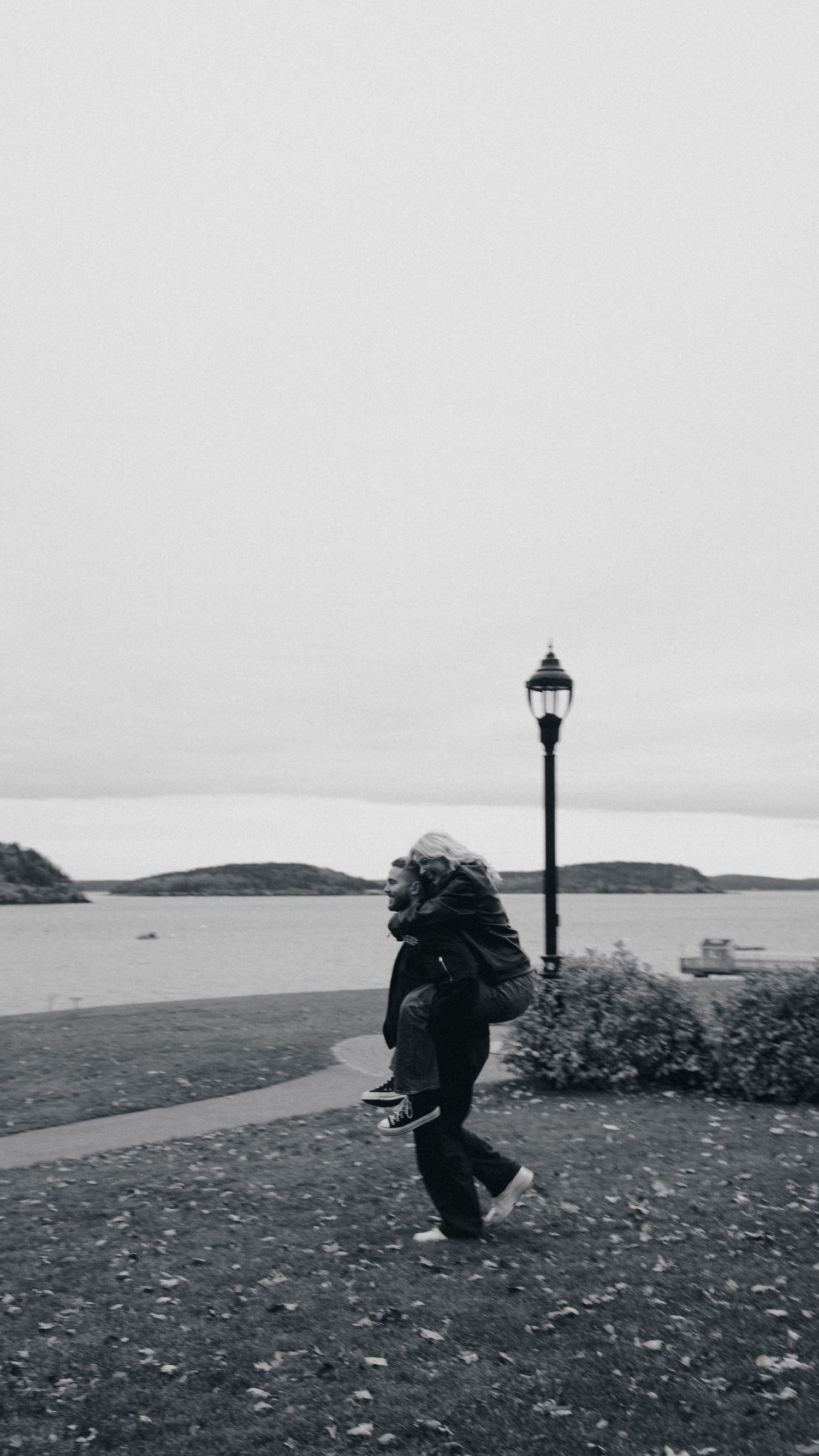 A silhouetted figure walks along a coastal path with a lamp post against an overcast sky and ocean view.Couple in Bar Harbor Maine