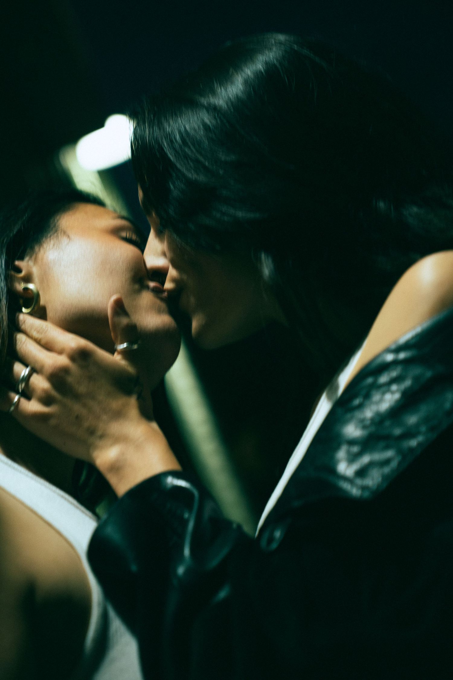 Two shadowy figures in silhouette share an intimate kiss in dramatic dark lighting.