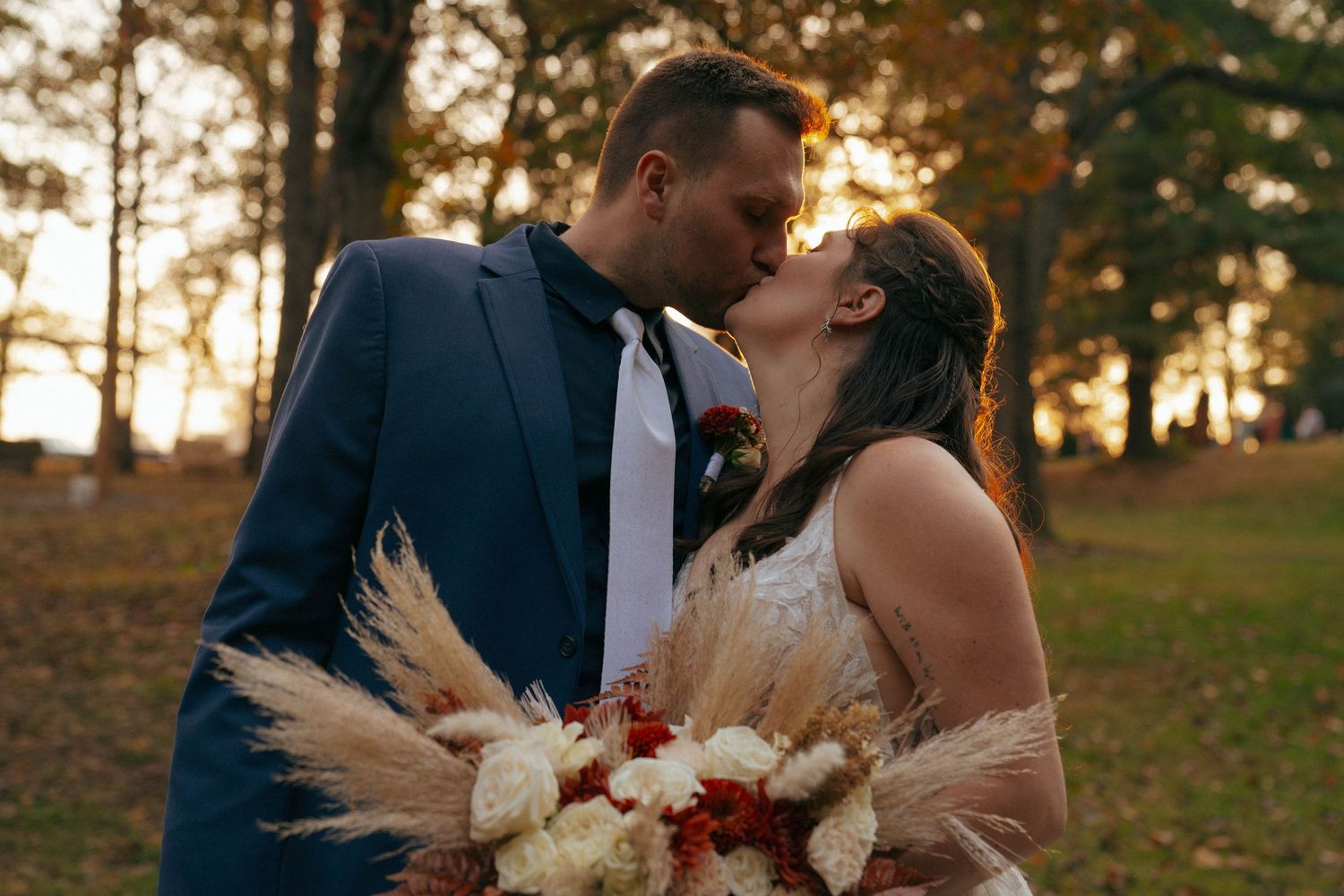 A romantic sunset kiss in a golden autumn field with a dried pampas grass wedding bouquet.