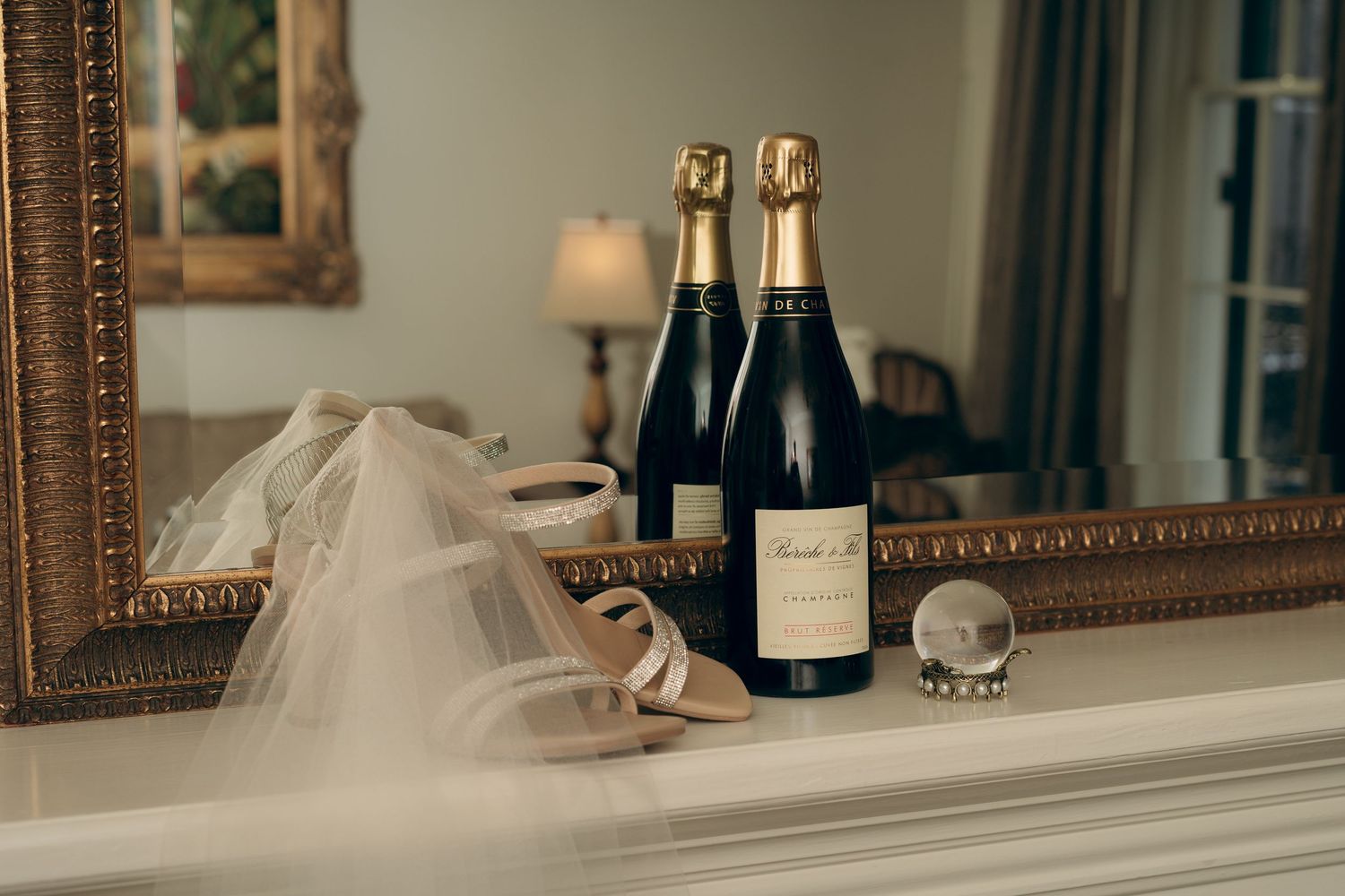 Wedding details arranged on a mantel including champagne bottles and a bridal veil in an elegant setting.