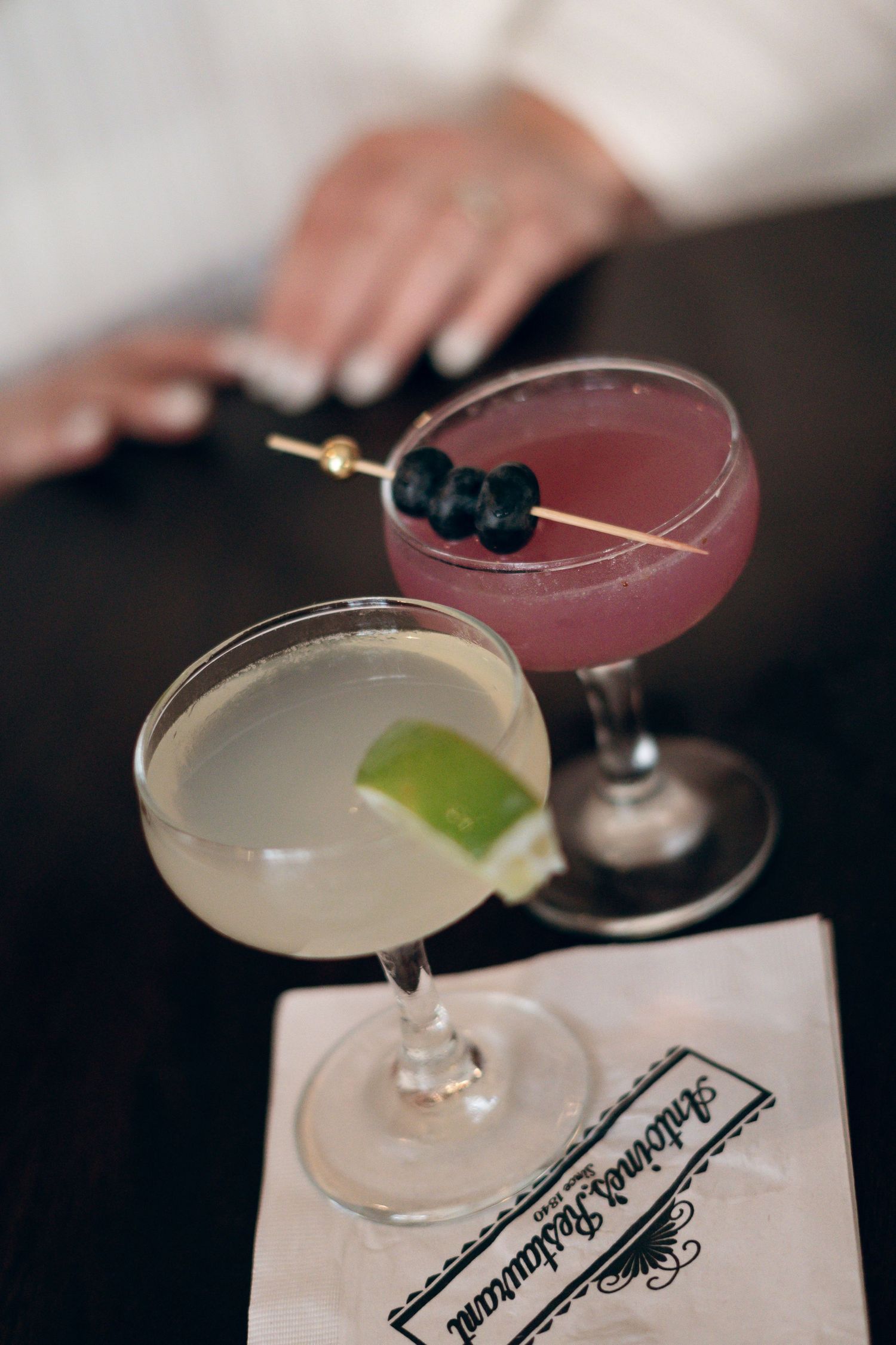 Elegant cocktails garnished with blueberries and lime on a dark bar counter.