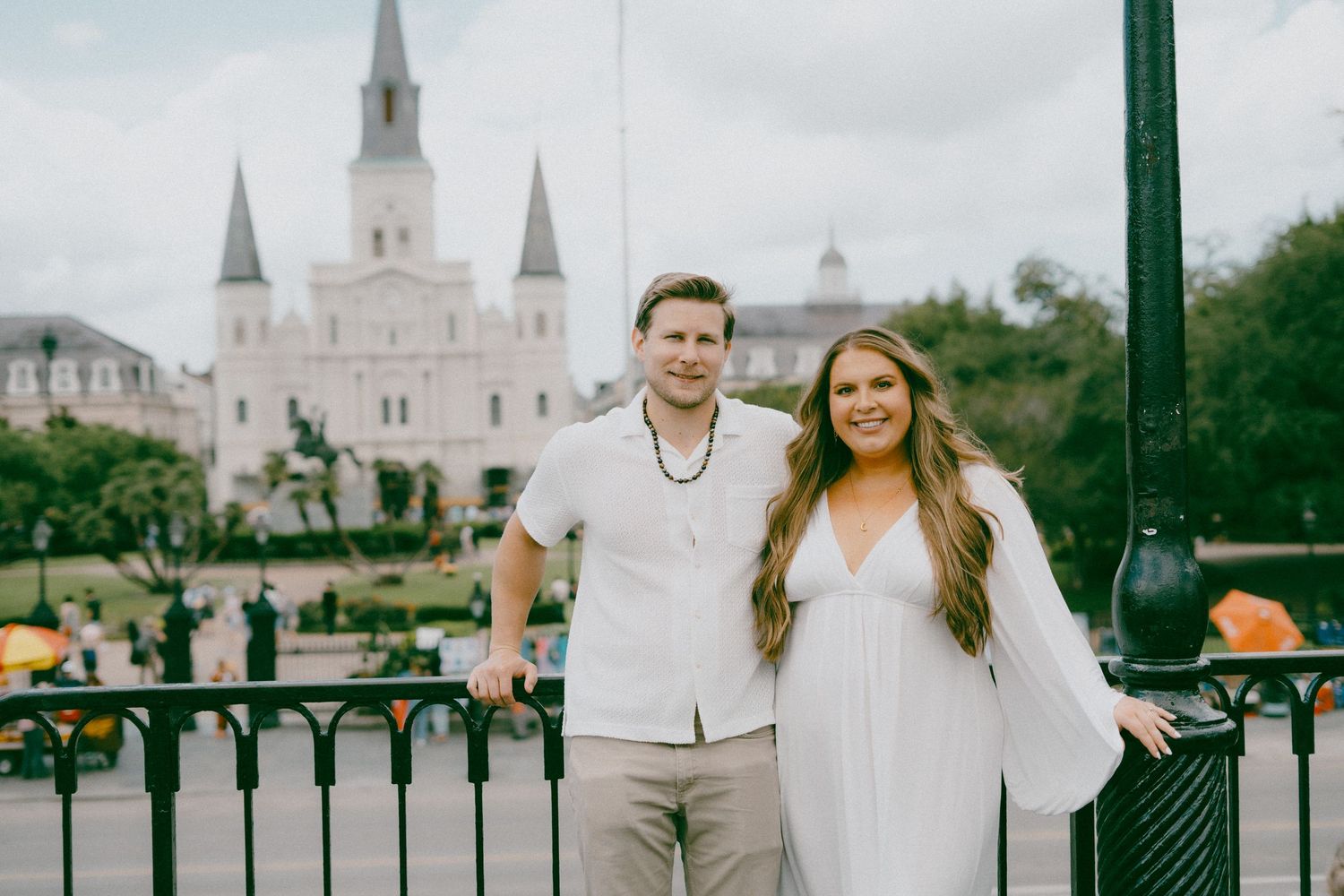 Two people in white outfits pose in Jackson Square with Saint Louis Cathedral in background in New Orleans.