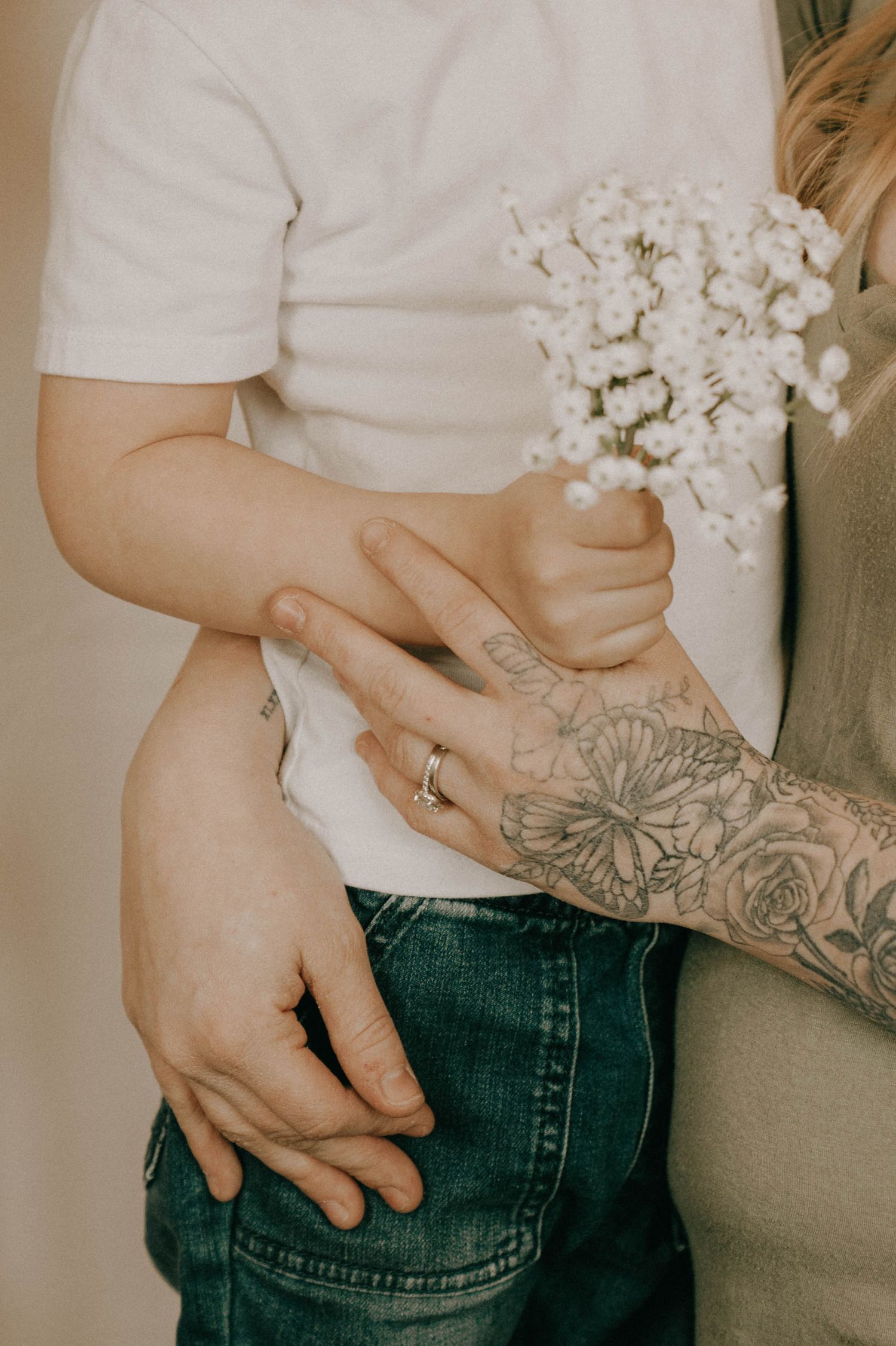 Close-up of hands holding white flowers, showing a tattoo and wedding ring.