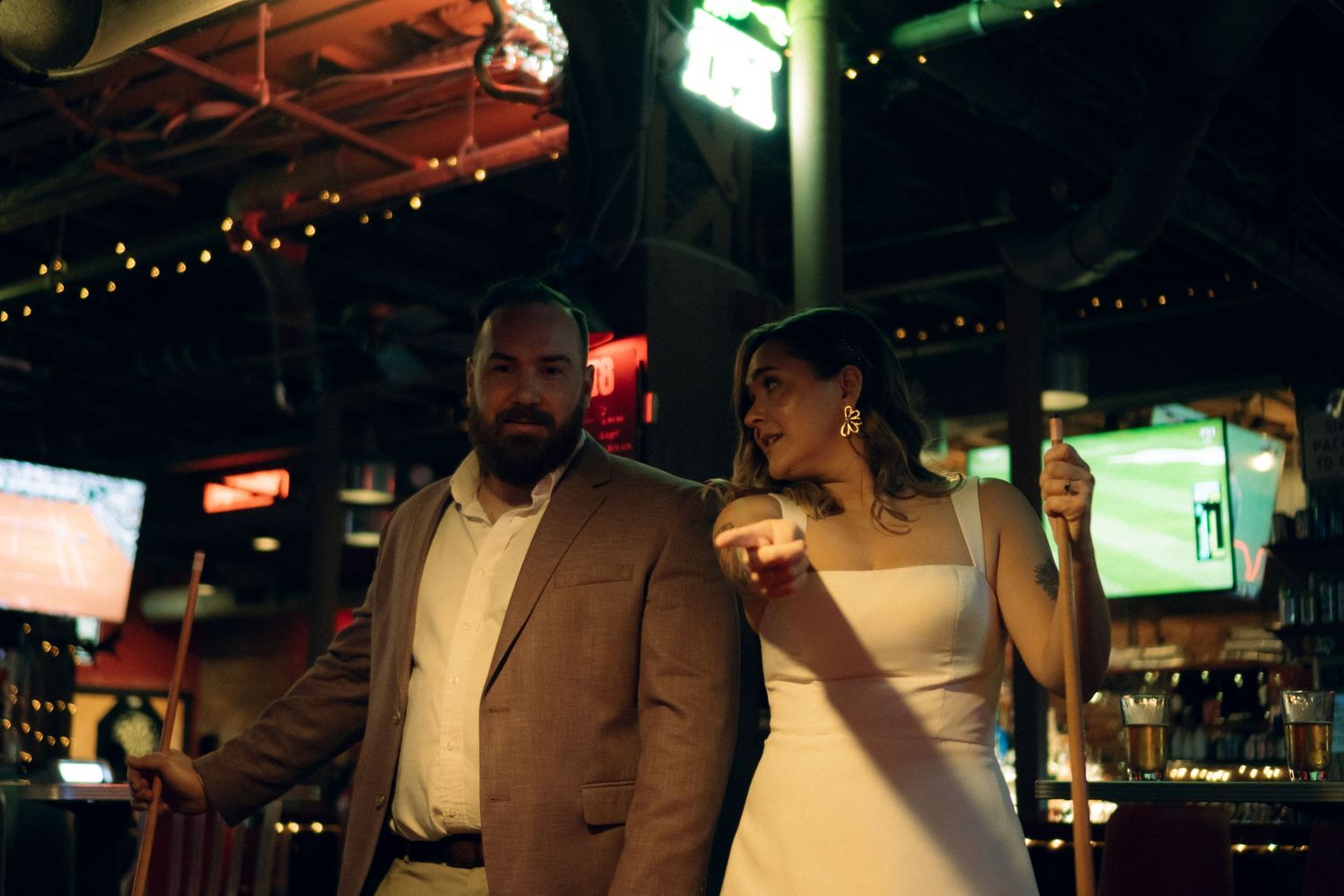 Two people laughing and enjoying drinks together at a dimly lit bar with string lights overhead. | Cinematic Photographer | Julianna Palumbo