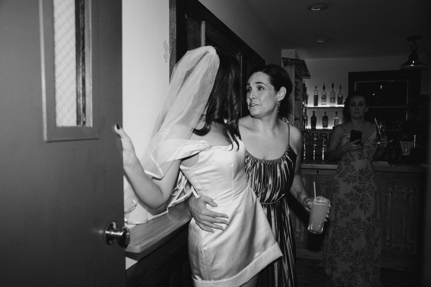 Two women in wedding attire sharing an intimate moment in a dimly lit venue.