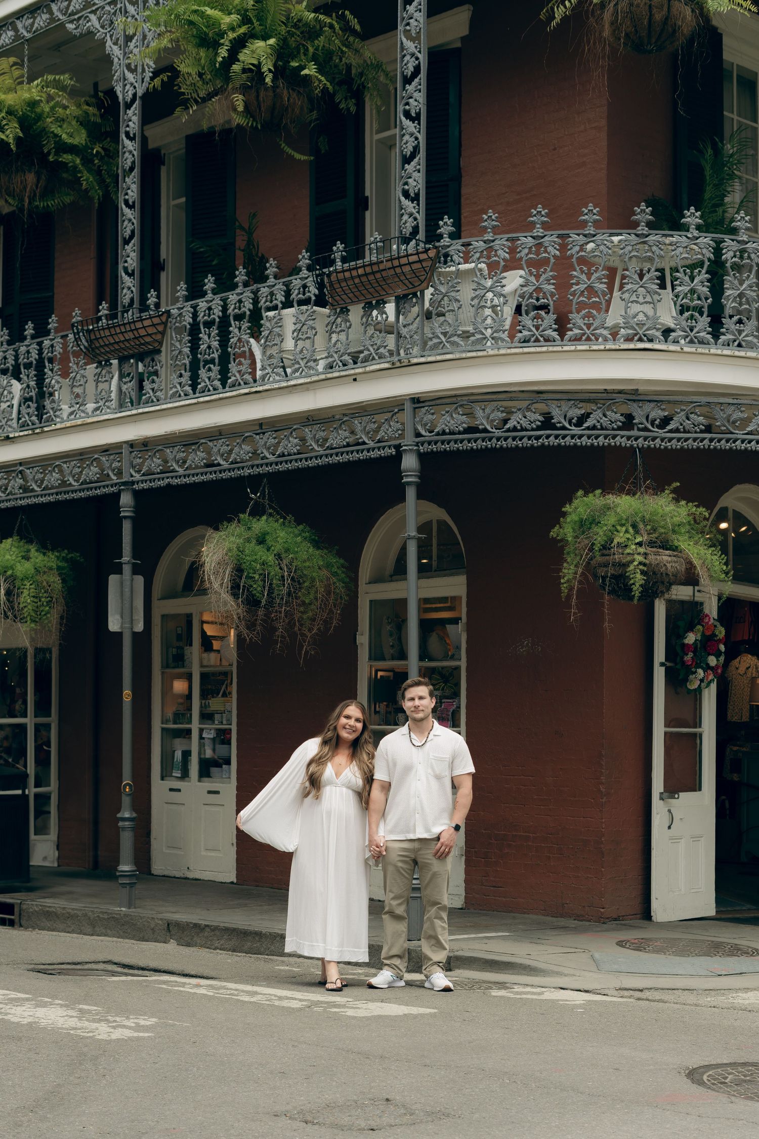 A couple poses in front of a historic building with ornate wrought iron balconies in New Orleans' French Quarter.