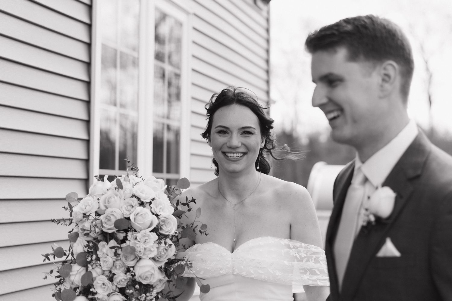 Black and white photo of a couple on their wedding day with the bride holding a beautiful floral bouquet.
