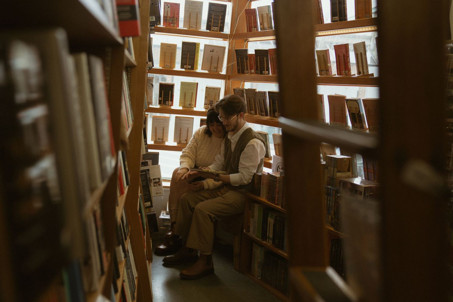 A person browses through books on wooden shelves in a cozy library with natural light streaming through windows.Couple in Bar Harbor Maine