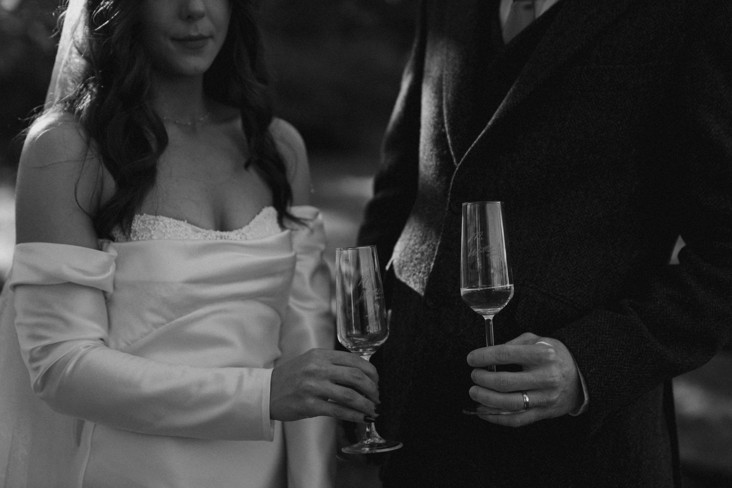 Black and white image of newlyweds holding champagne glasses during celebration.