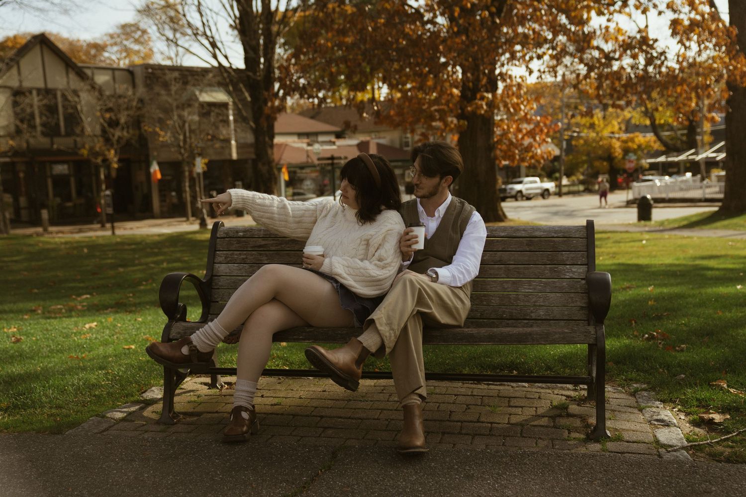 A couple sits together on stone steps in a park during autumn with golden leaves scattered around them. Couple in Bar Harbor Maine