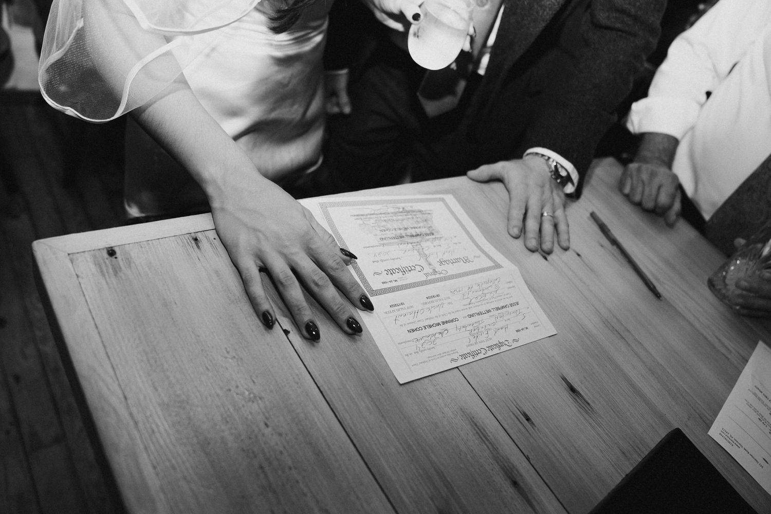 Hands placing or reviewing documents on a wooden table in black and white.