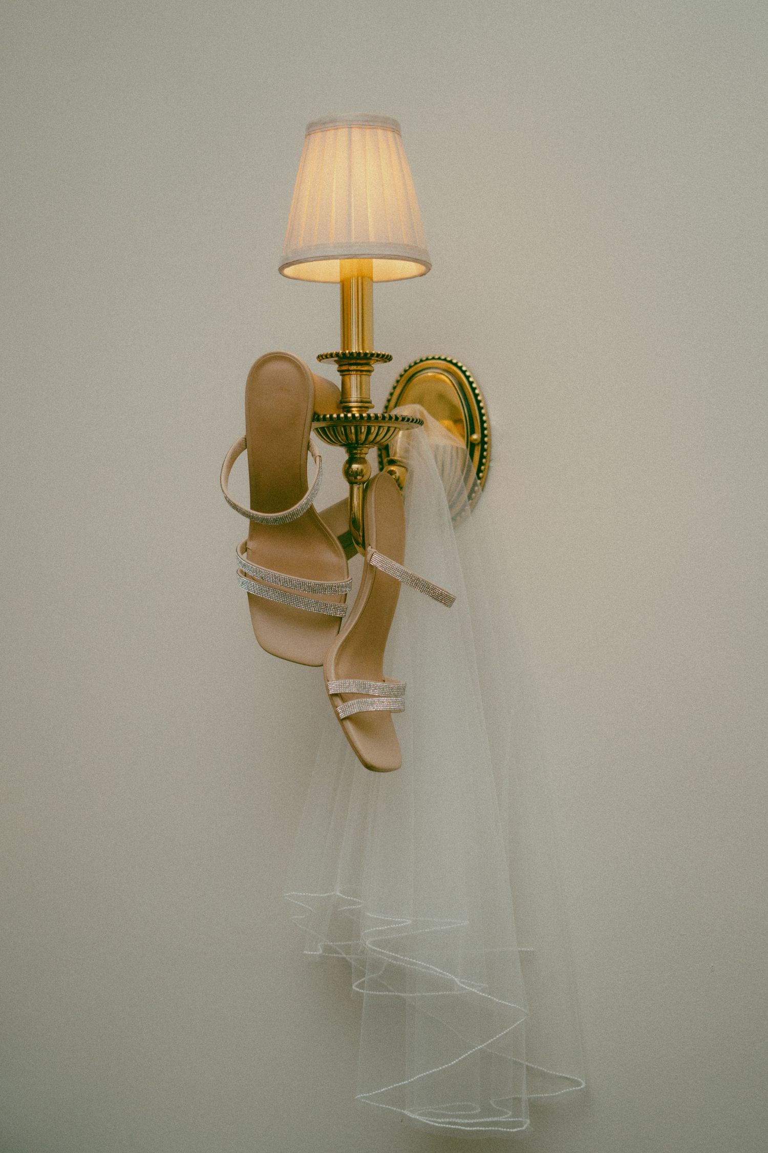 Wedding shoes and veil elegantly displayed hanging from a wall-mounted brass lamp sconce.