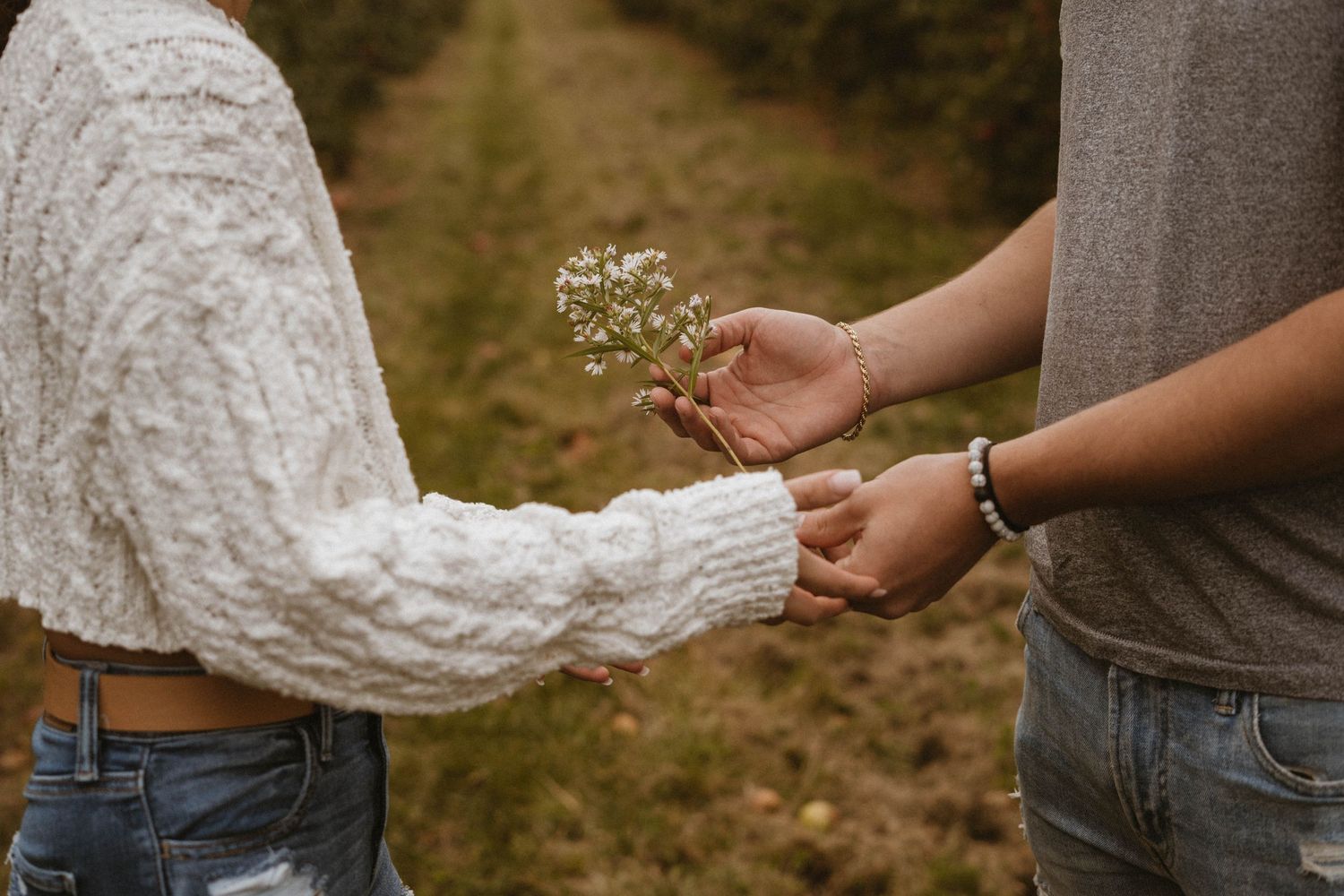 Hands exchanging small white flowers in a romantic outdoor setting.