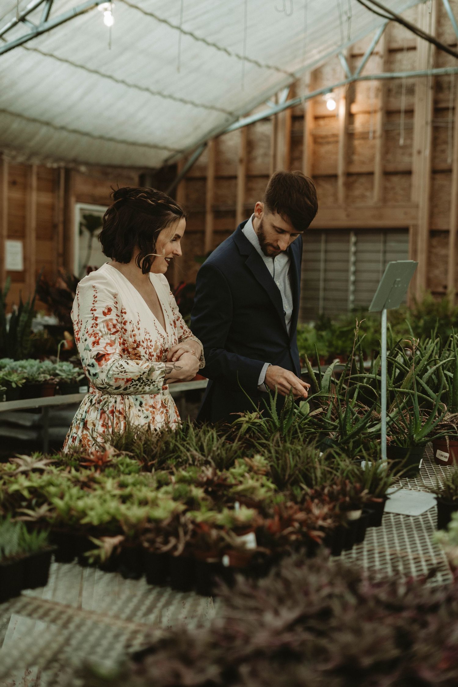 Two people browse through plants in a rustic greenhouse setting.
