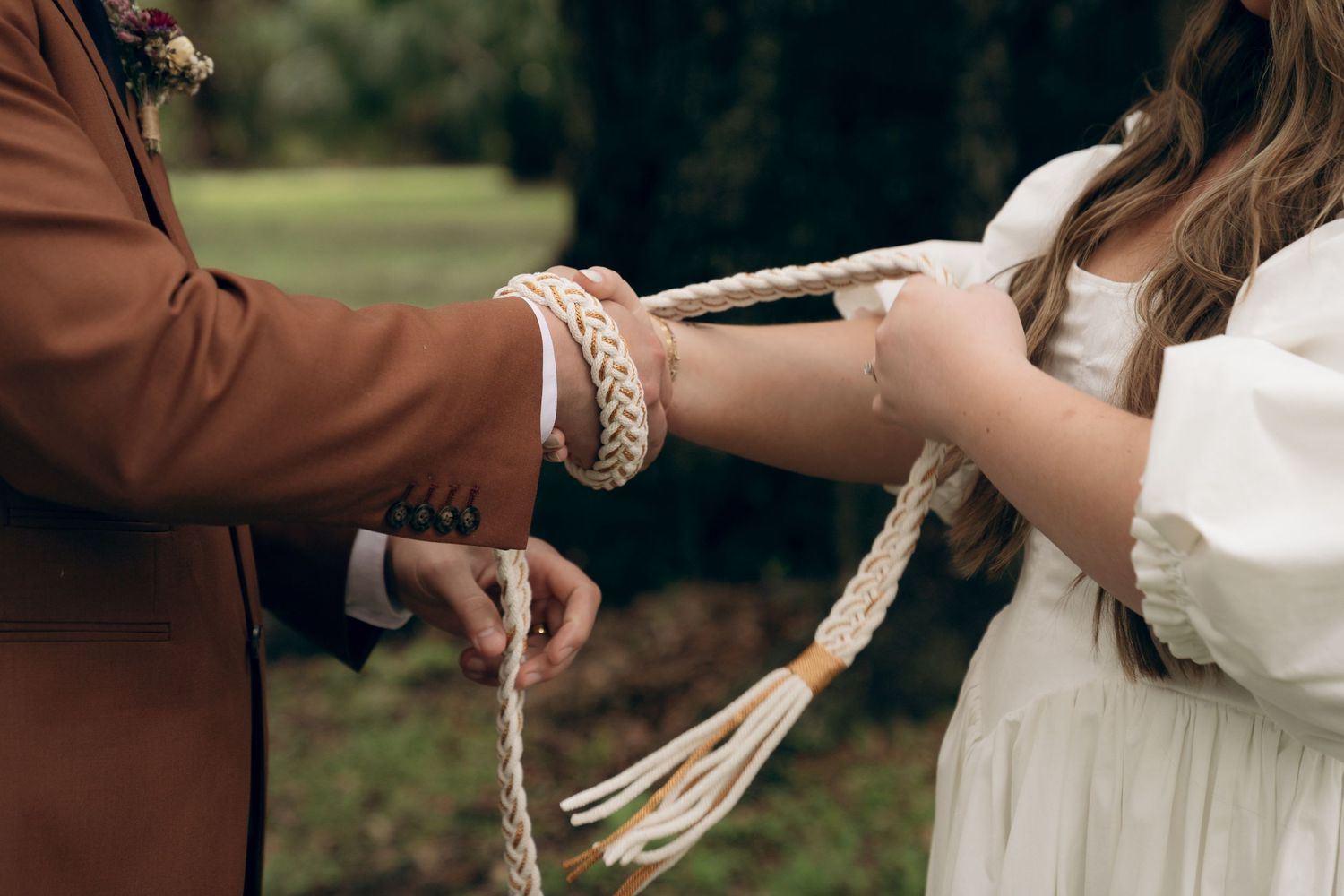 A couple in brown and white attire share an intimate moment outdoors in a garden setting.