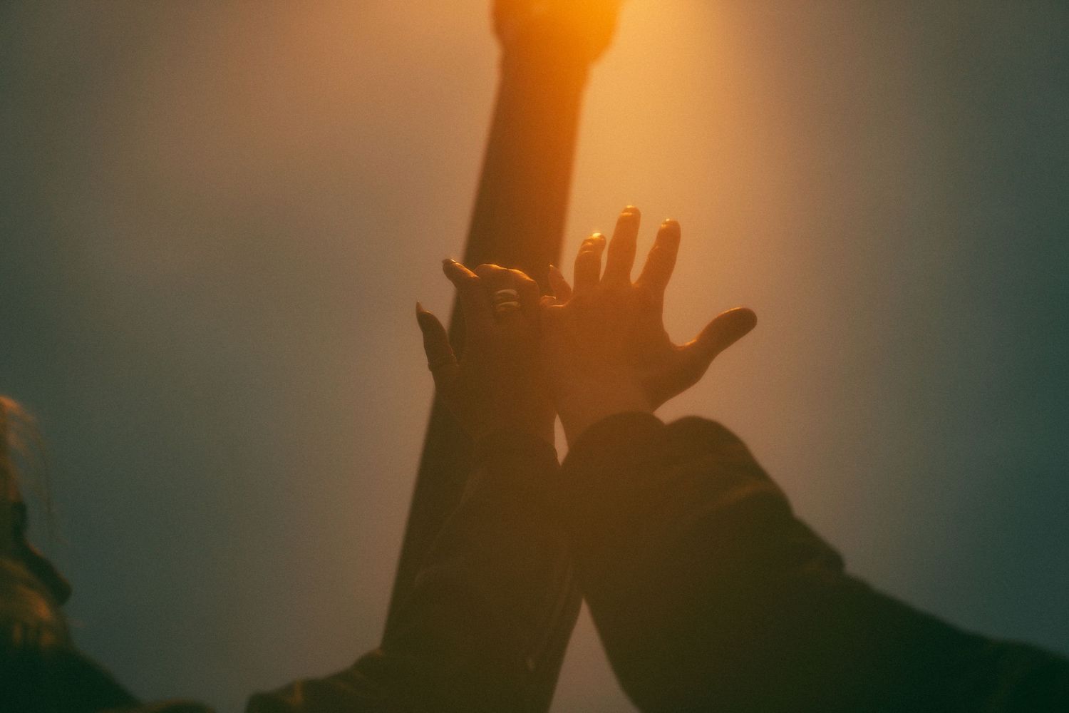 A silhouetted hand reaches up towards a glowing light source against a moody sunset sky.Couple in Bar Harbor Maine
