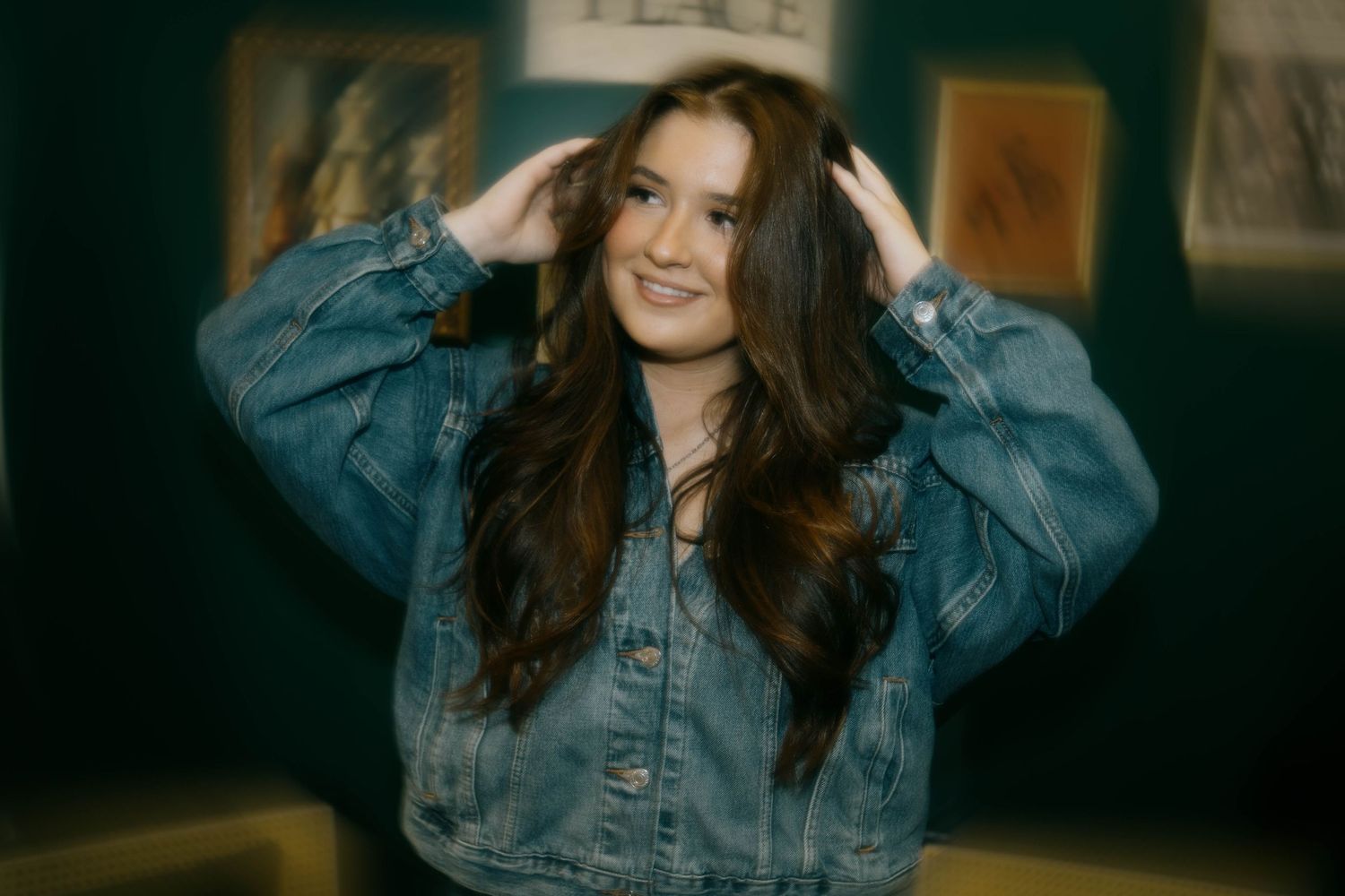 Portrait of someone in a denim jacket posing against a dark background.