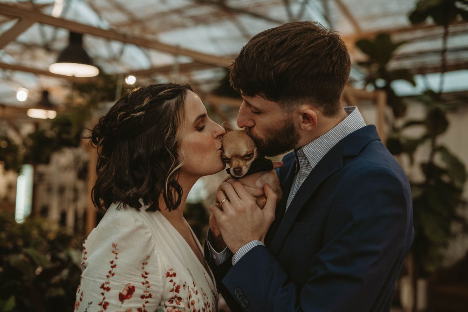 A romantic moment captured in a greenhouse setting with moody lighting and natural decor.