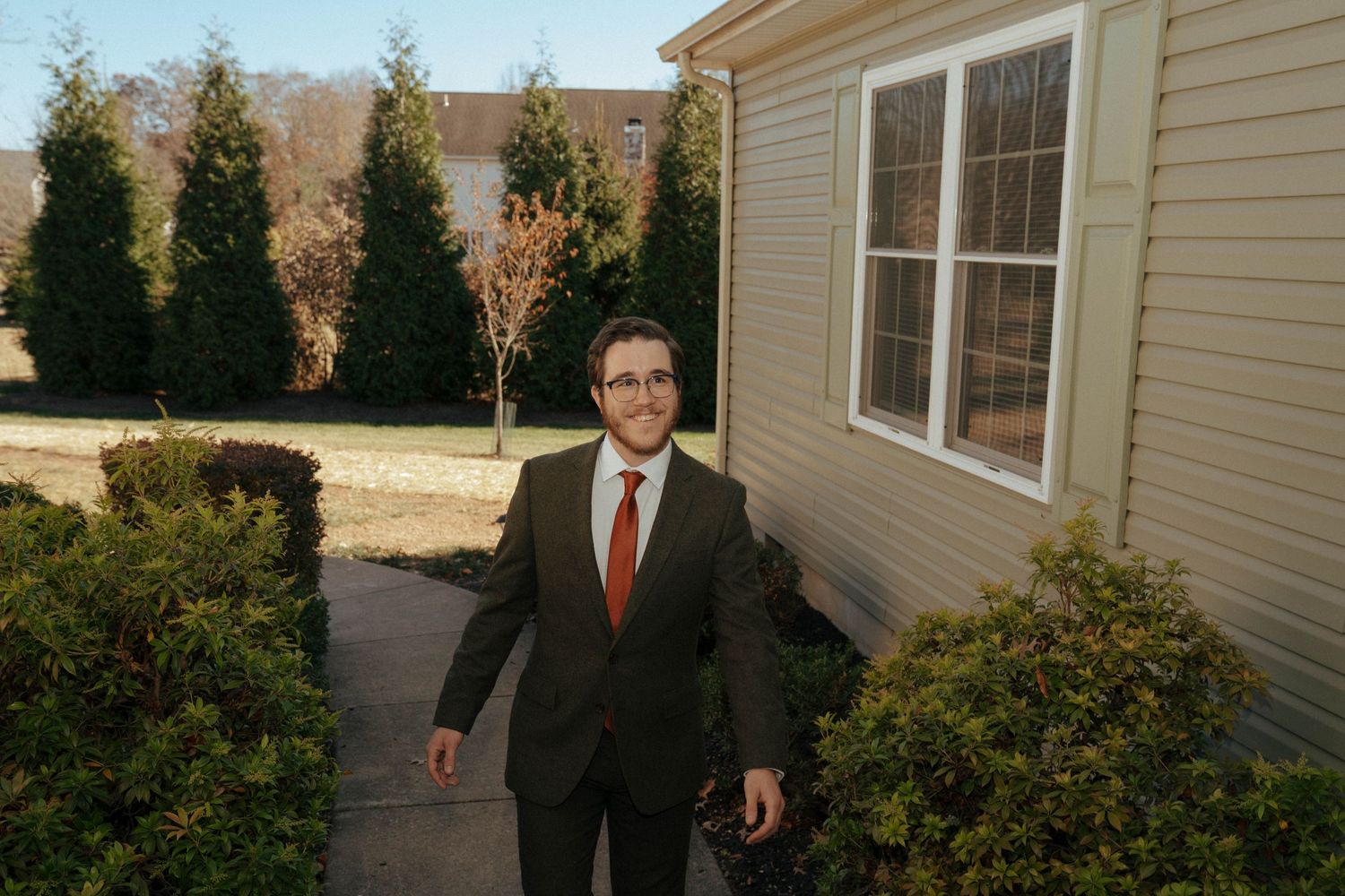 Formal attire against backdrop of landscaped yard with evergreen trees.