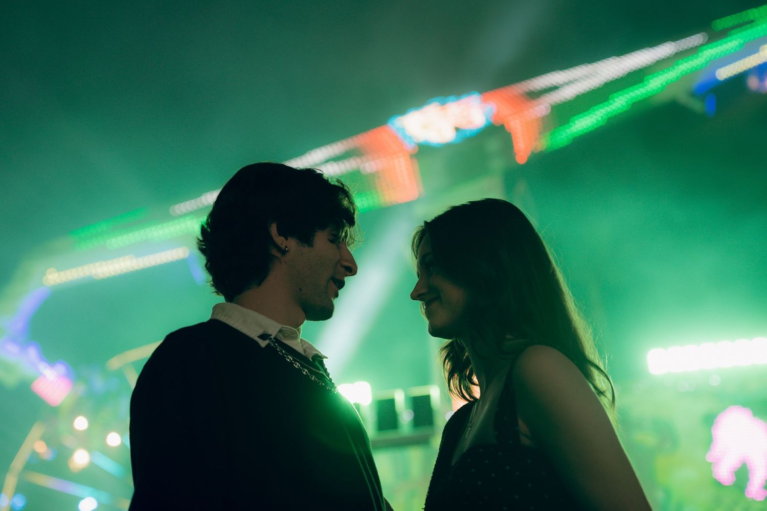 A couple shares an intimate moment on a dance floor illuminated by vibrant green lights and party decorations.