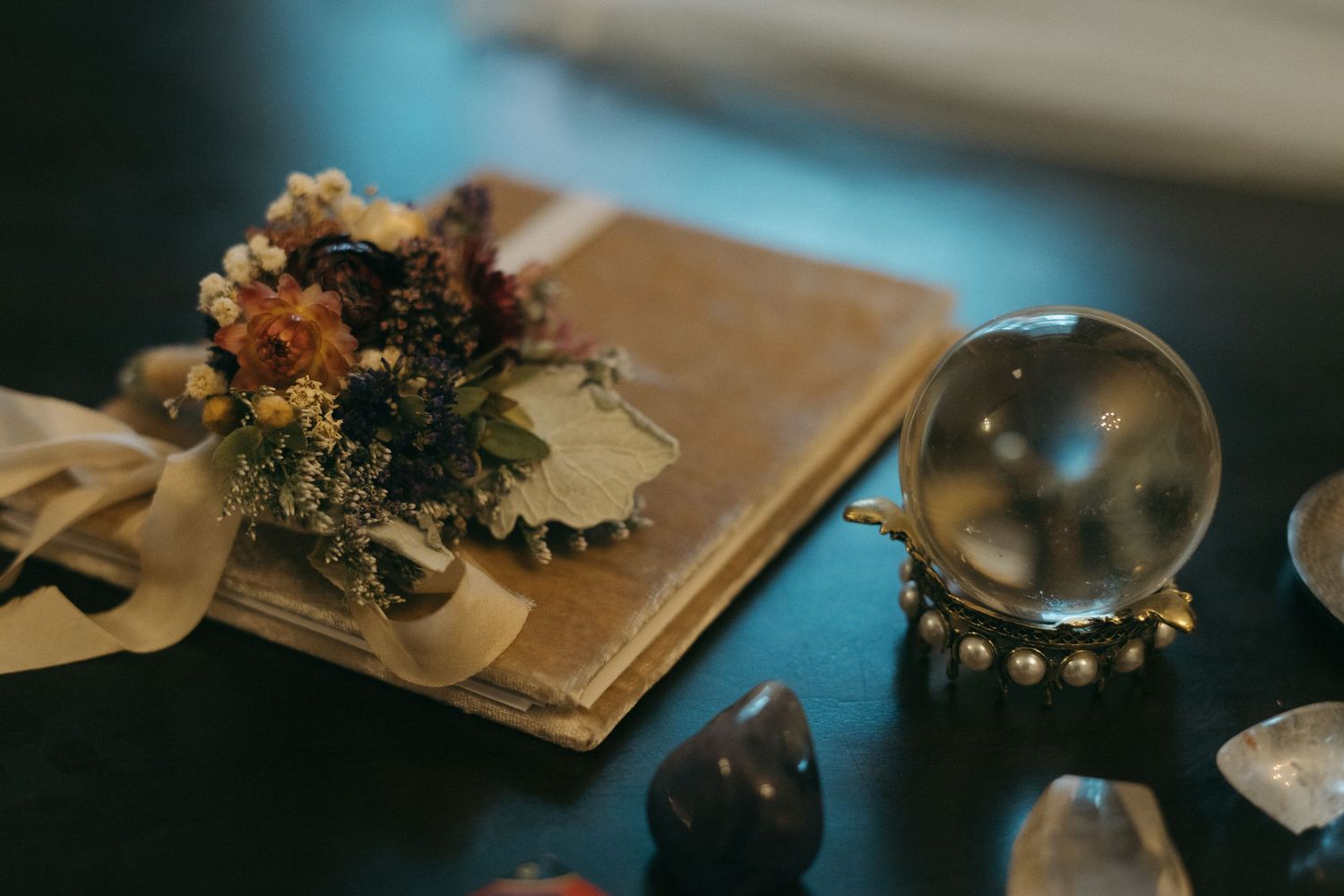 A mystical still life with dried flowers, old papers and a crystal ball on a dark surface.