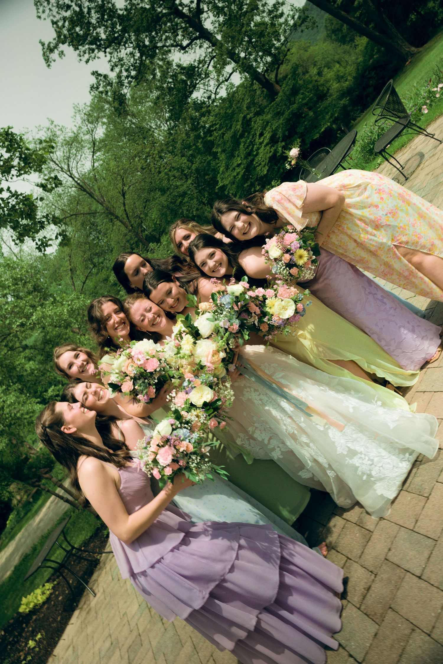 Bridesmaids in lavender dresses pose with colorful floral bouquets against a garden backdrop.
