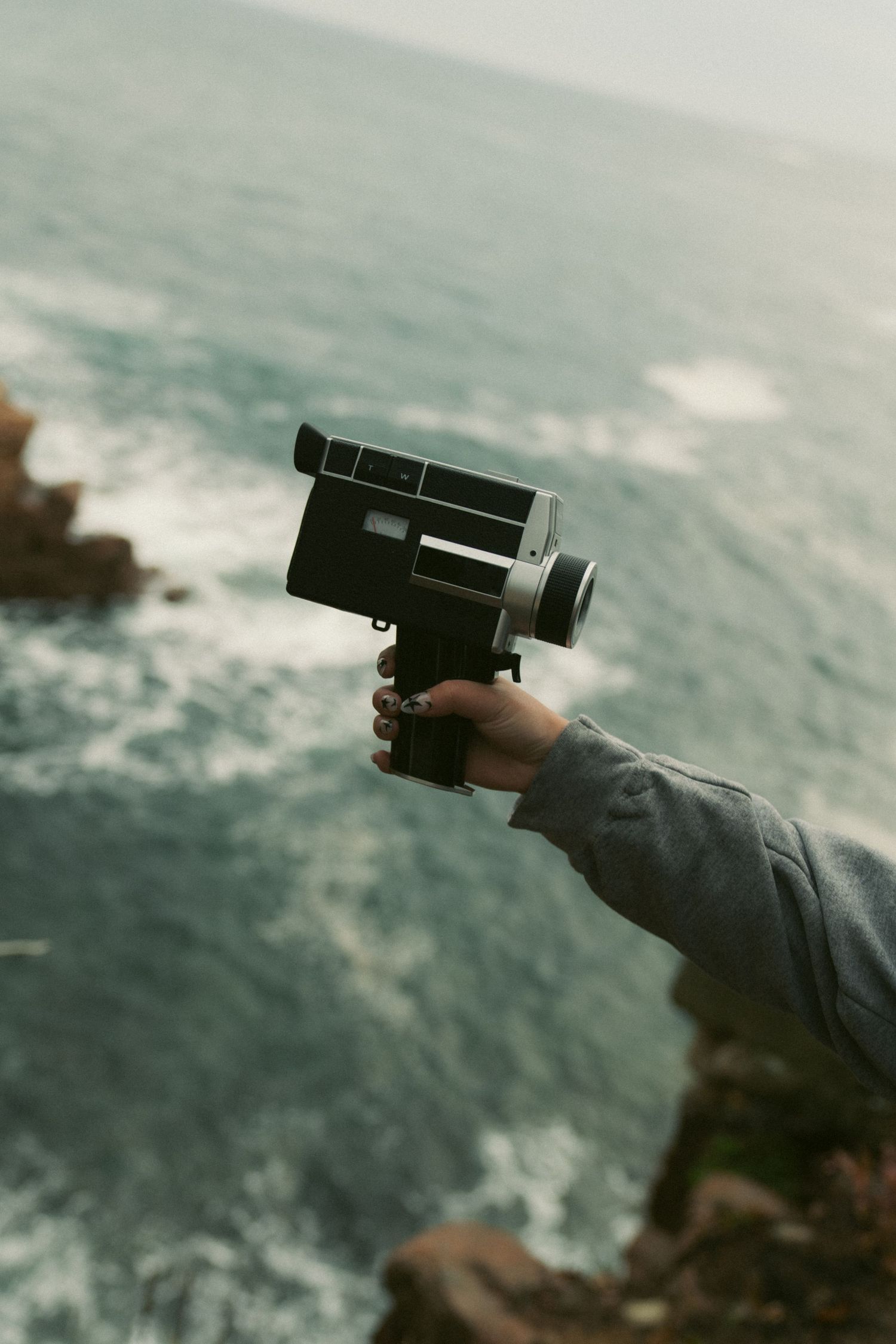 A hand holds a dark pistol pointed towards the ocean against a moody seascape backdrop.