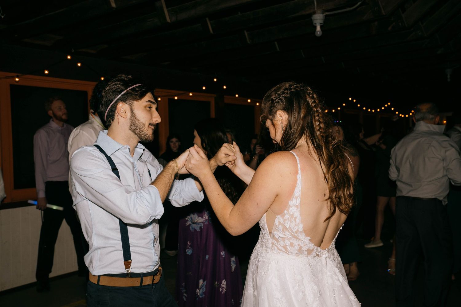 A couple dancing together at a dimly lit wedding reception with string lights overhead.