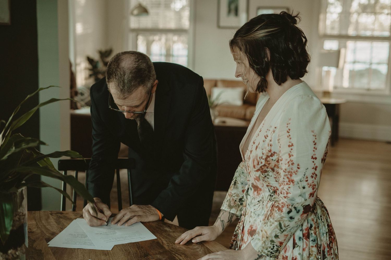 Two people review and sign documents together at a wooden table.