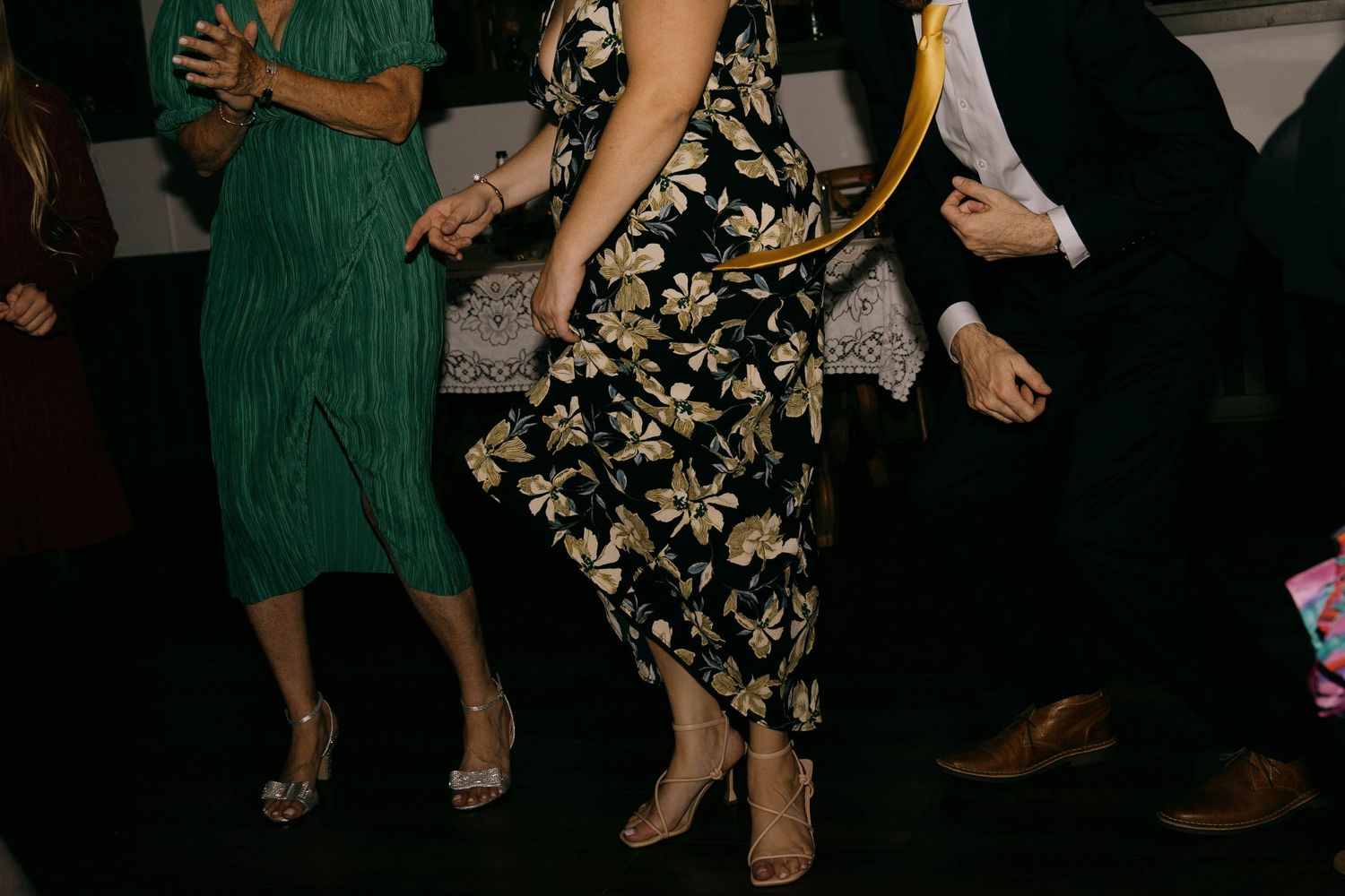 Wedding guests dancing, showing colorful dresses and formal attire from waist down.