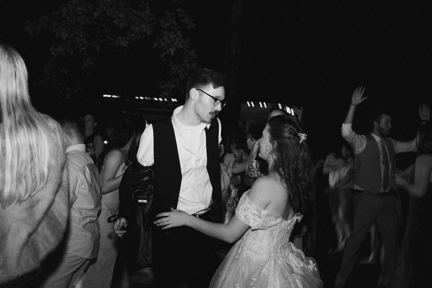 Wedding guests dancing at a nighttime reception while the newlyweds share a special moment on the dance floor.