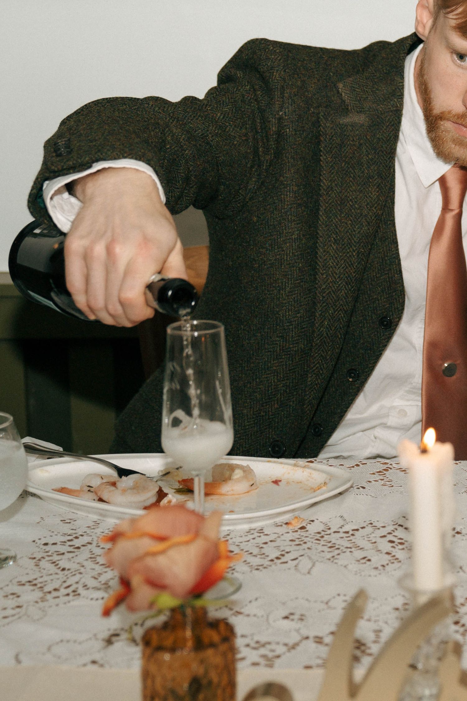 Someone pours a beverage into a glass at an elegant candlelit table setting.
