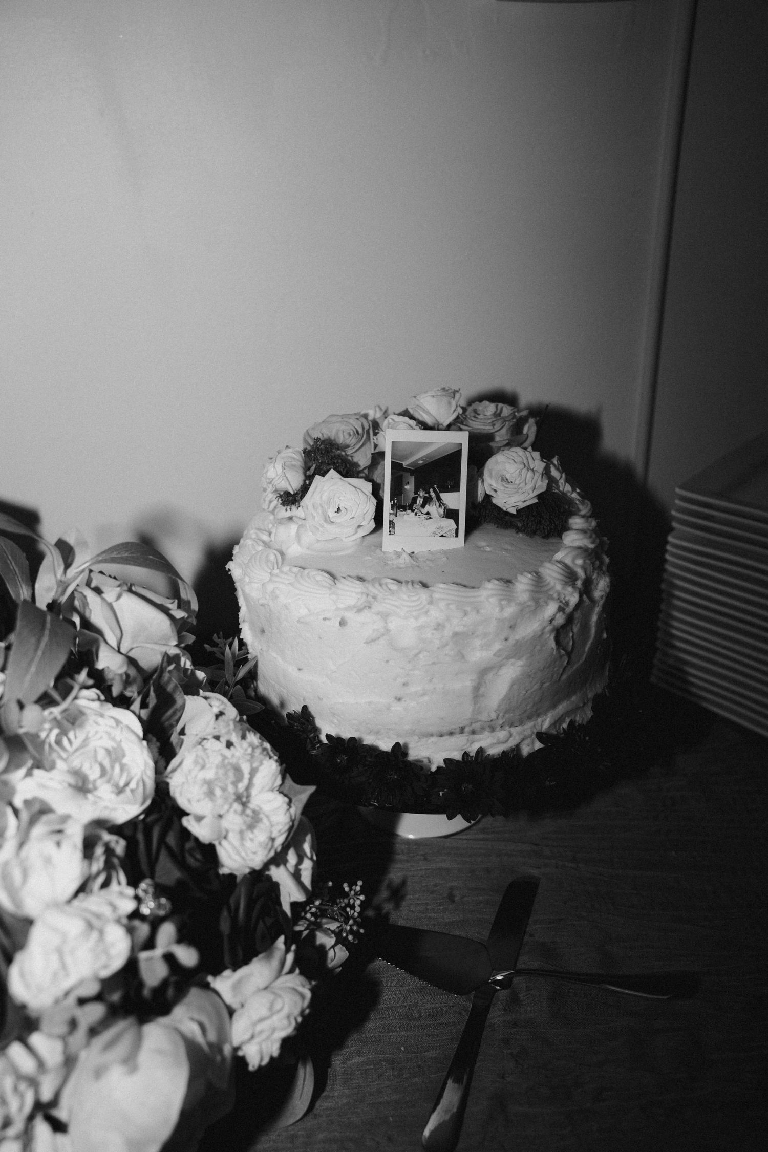 Black and white photo of decorated cake with flowers on wooden table.