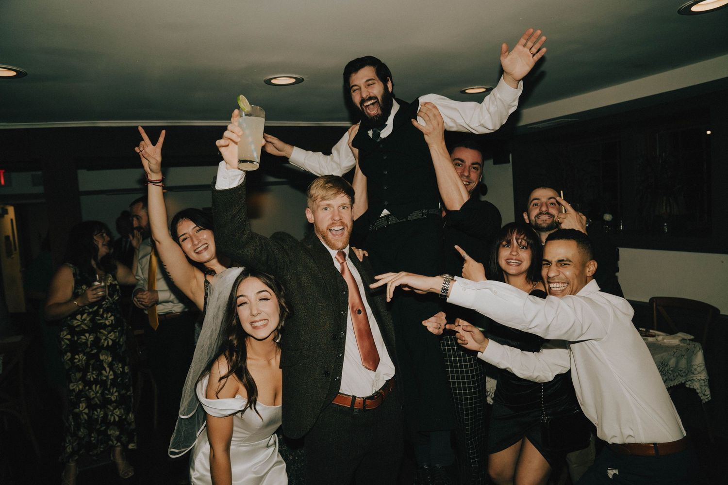 Lively wedding reception scene with guests celebrating and raising their arms in joy.