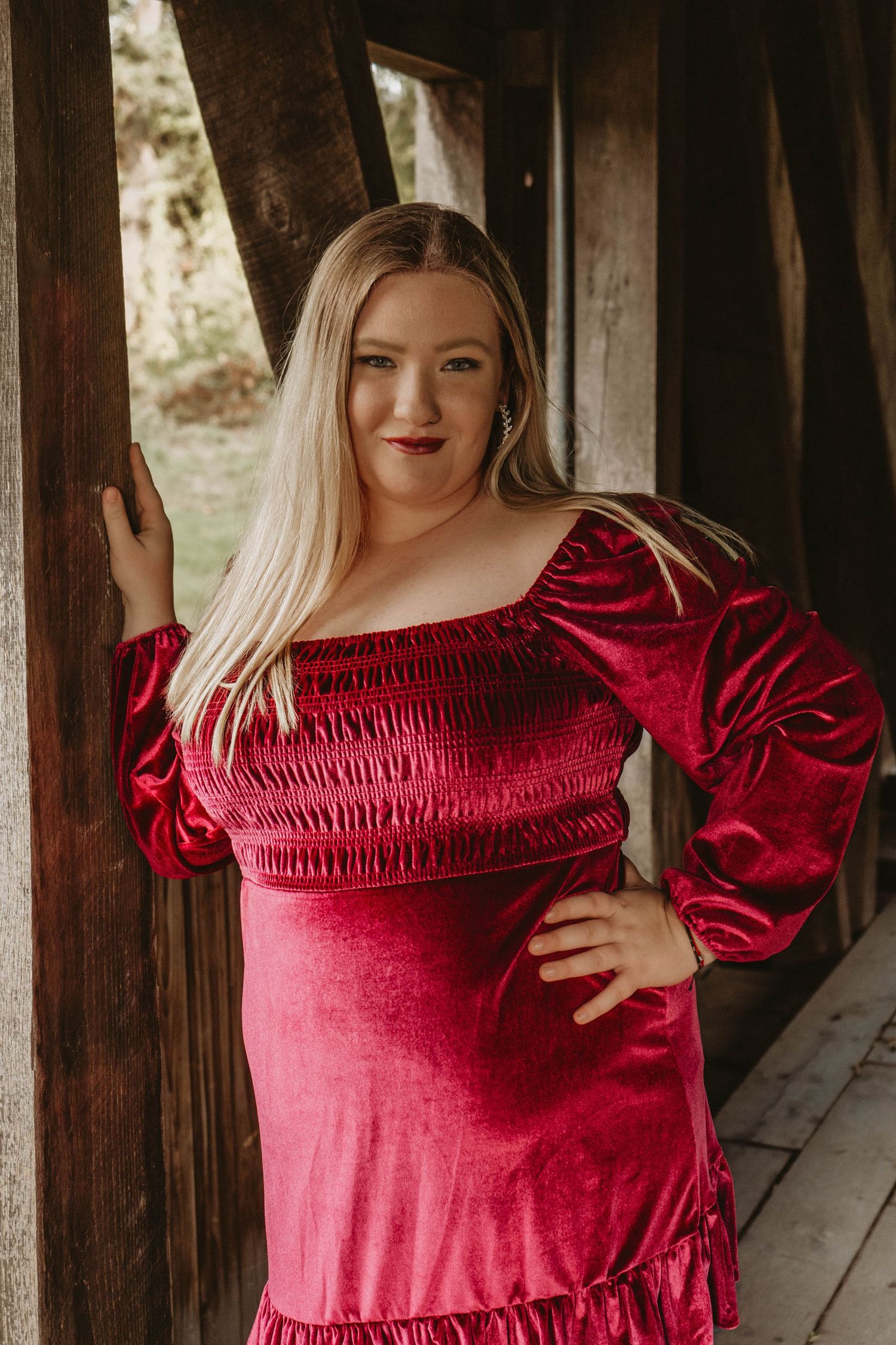Portrait in red velvet dress with puffy sleeves against wooden backdrop.