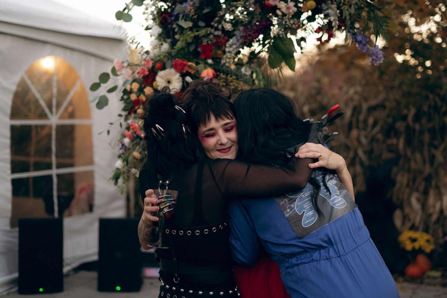 A couple embraces under autumn foliage and holiday lights during an outdoor evening celebration.