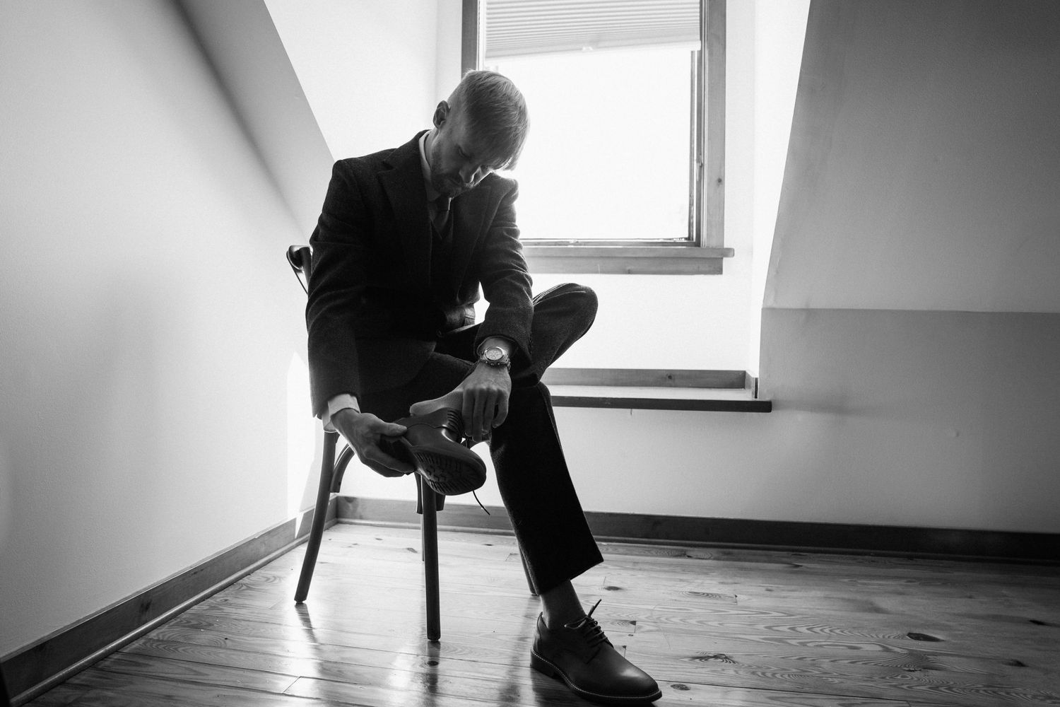 A minimalist black and white portrait of someone sitting on a stool by a window.