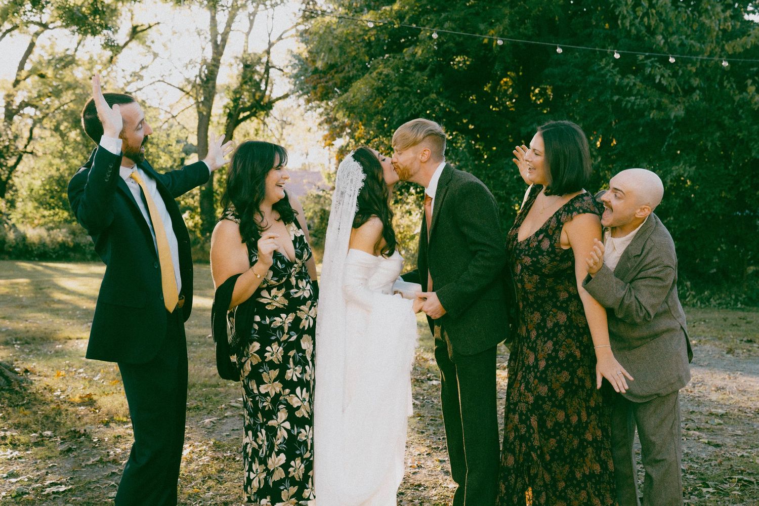 Wedding party poses together for a casual photo in an outdoor setting.