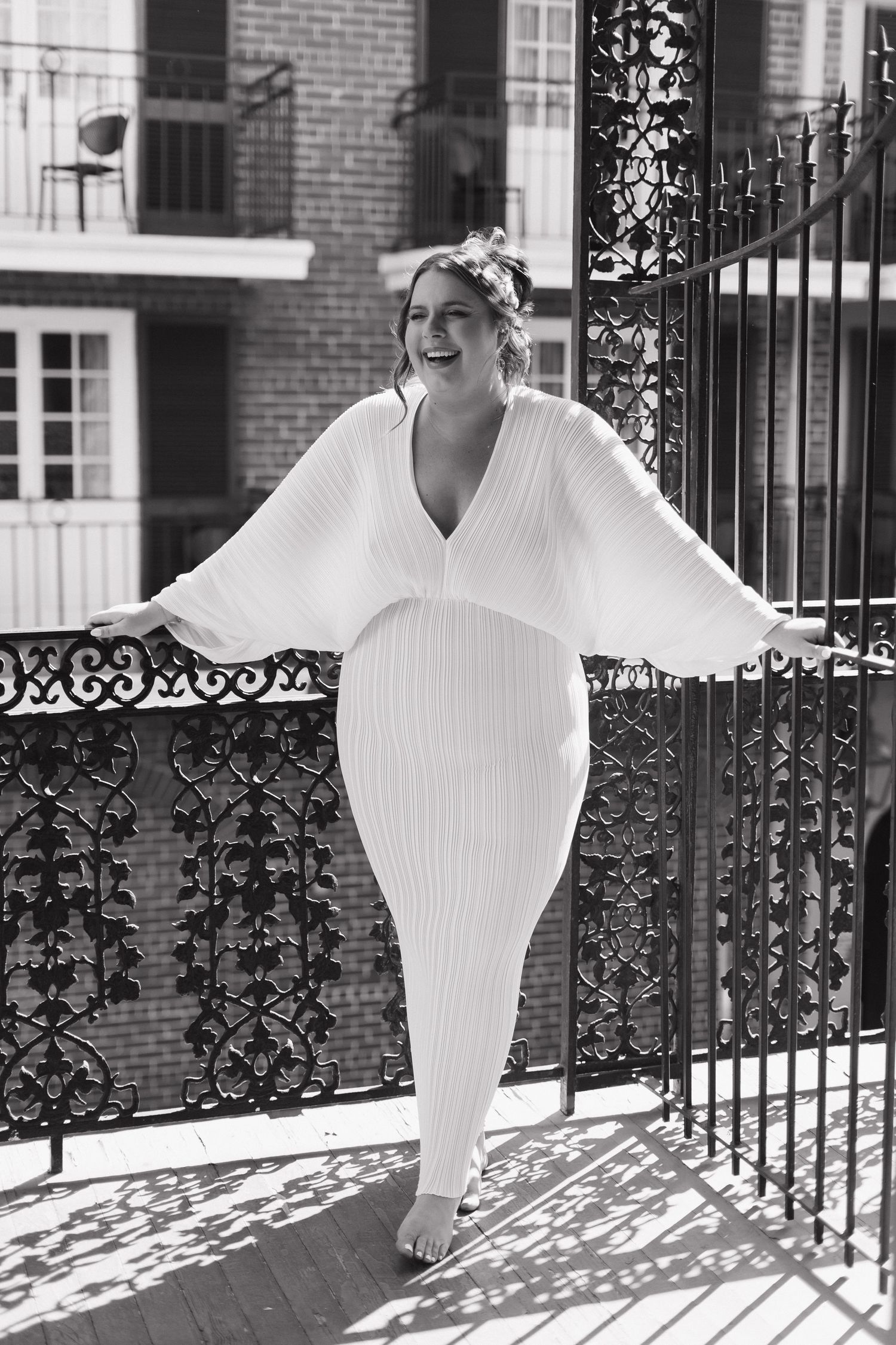 A bride in a flowing white dress with dramatic bell sleeves poses elegantly against an ornate wrought iron gate.