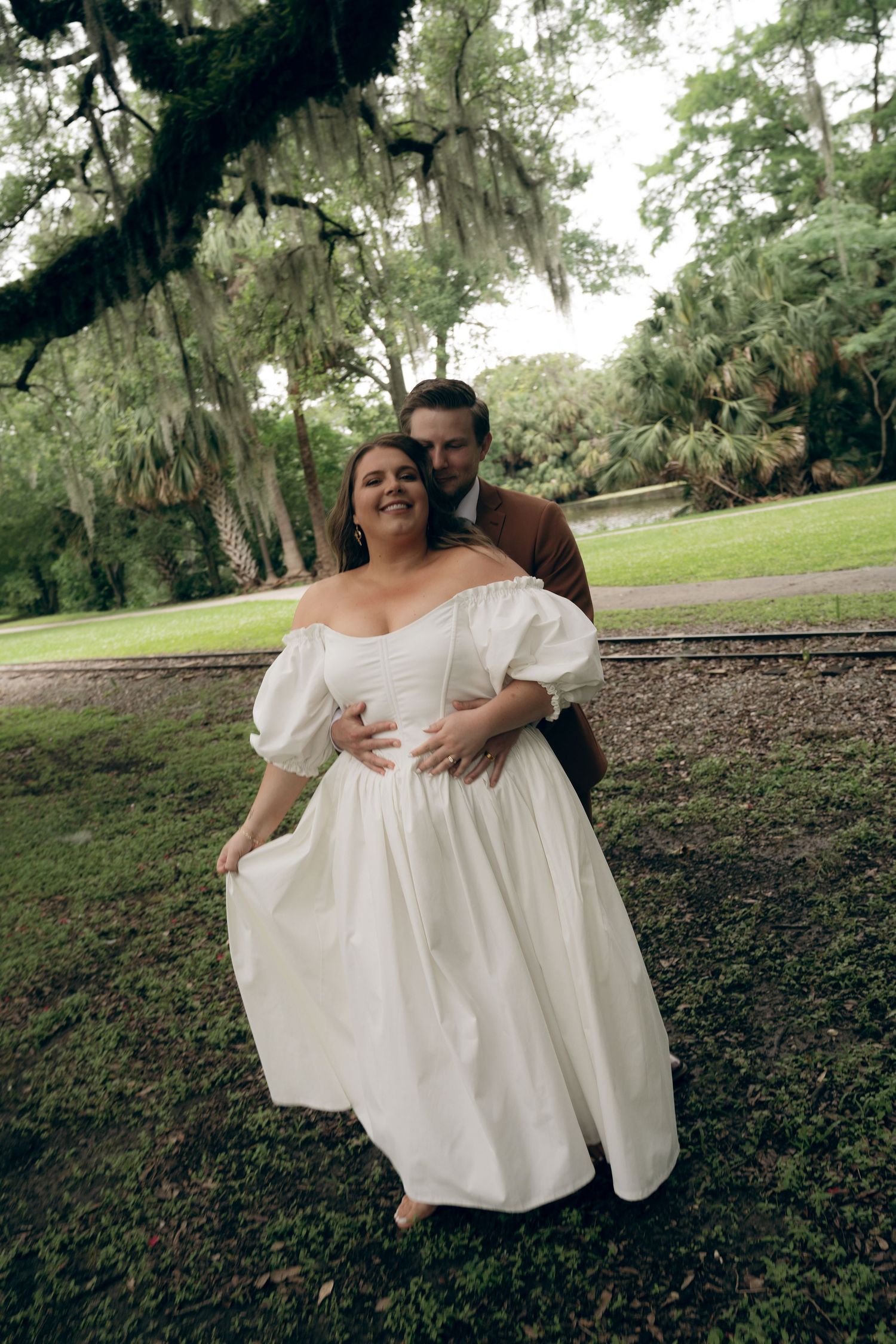 A couple shares an intimate moment together in a park setting surrounded by trees and natural scenery.