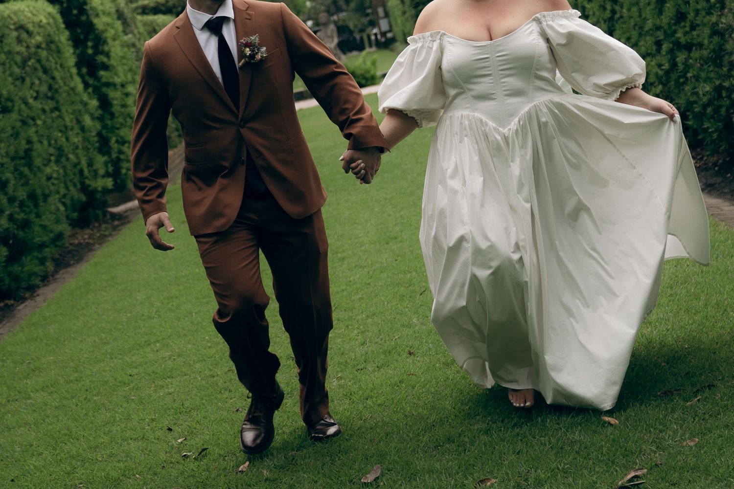 Newlyweds joyfully running across a lush green lawn during their wedding celebration.