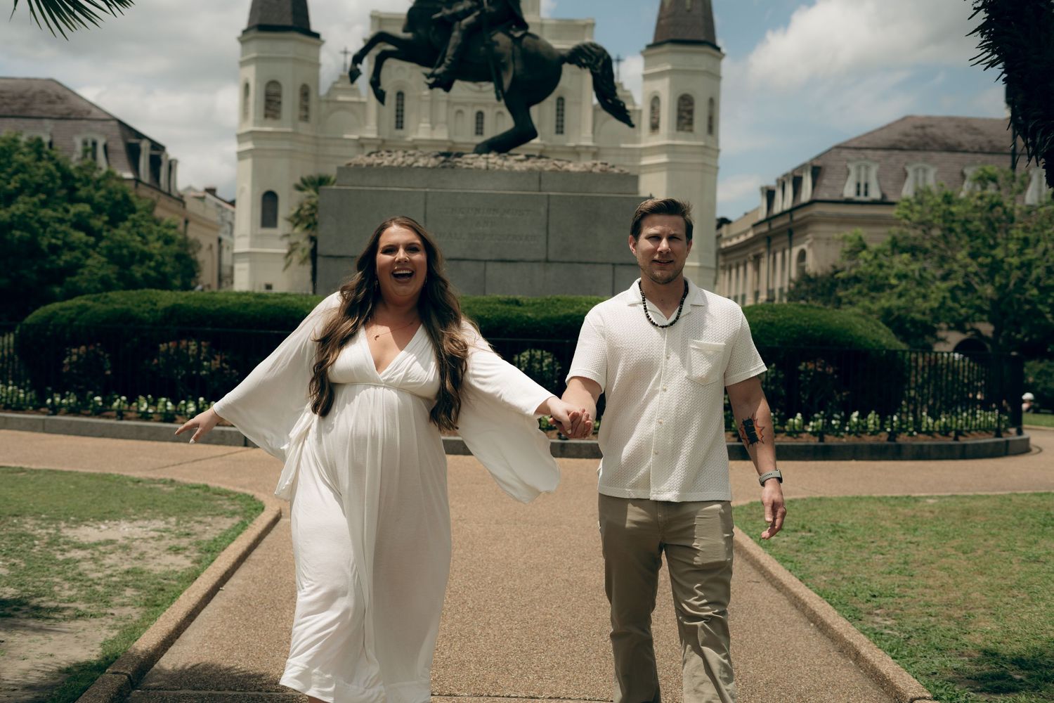 A couple walks hand in hand on a path in Jackson Square New Orleans with St. Louis Cathedral in the background.