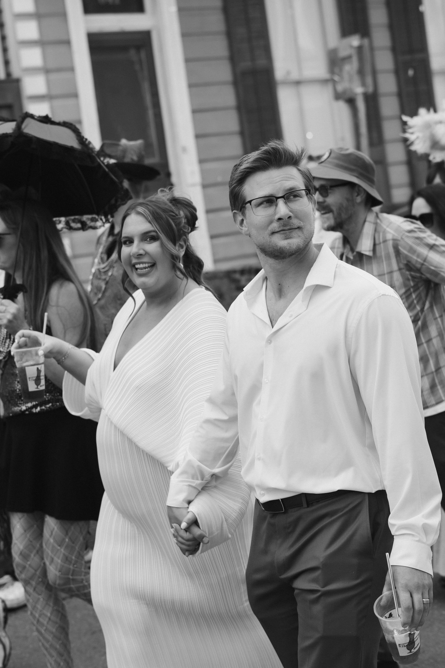 A couple dressed in white attire enjoys a festive outdoor celebration with other guests in a candid black and white photo.