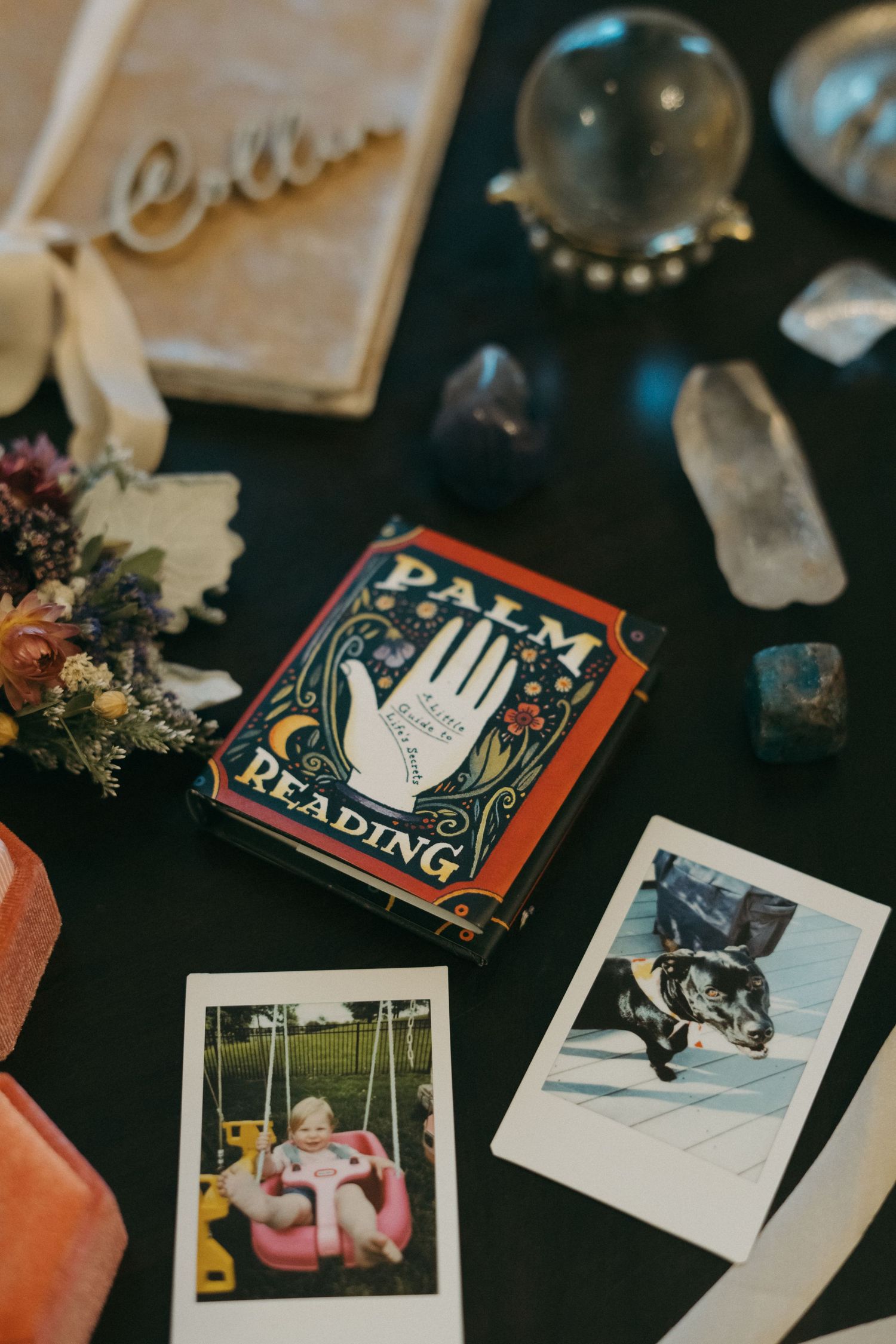 A mystical flat lay with palm reading cards, crystals, dried flowers, and vintage polaroid photos arranged on a dark surface.