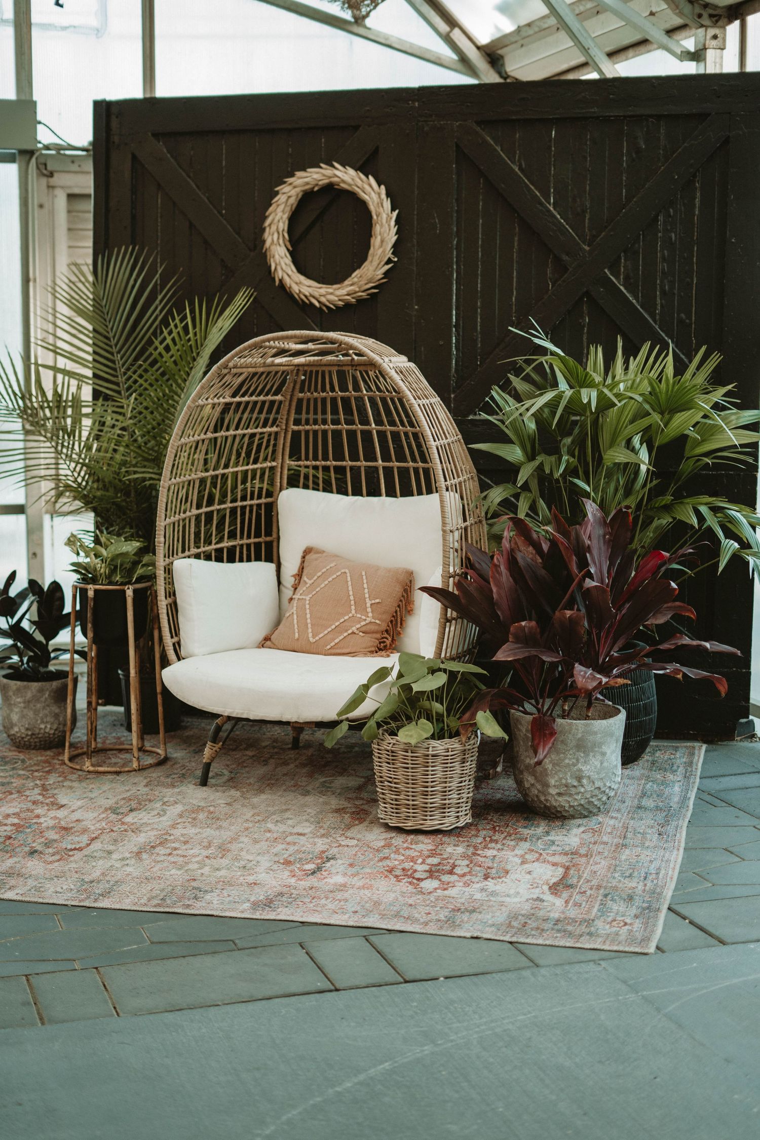 Cozy bohemian seating area with hanging egg chair, plants, and woven decor against black barn doors.