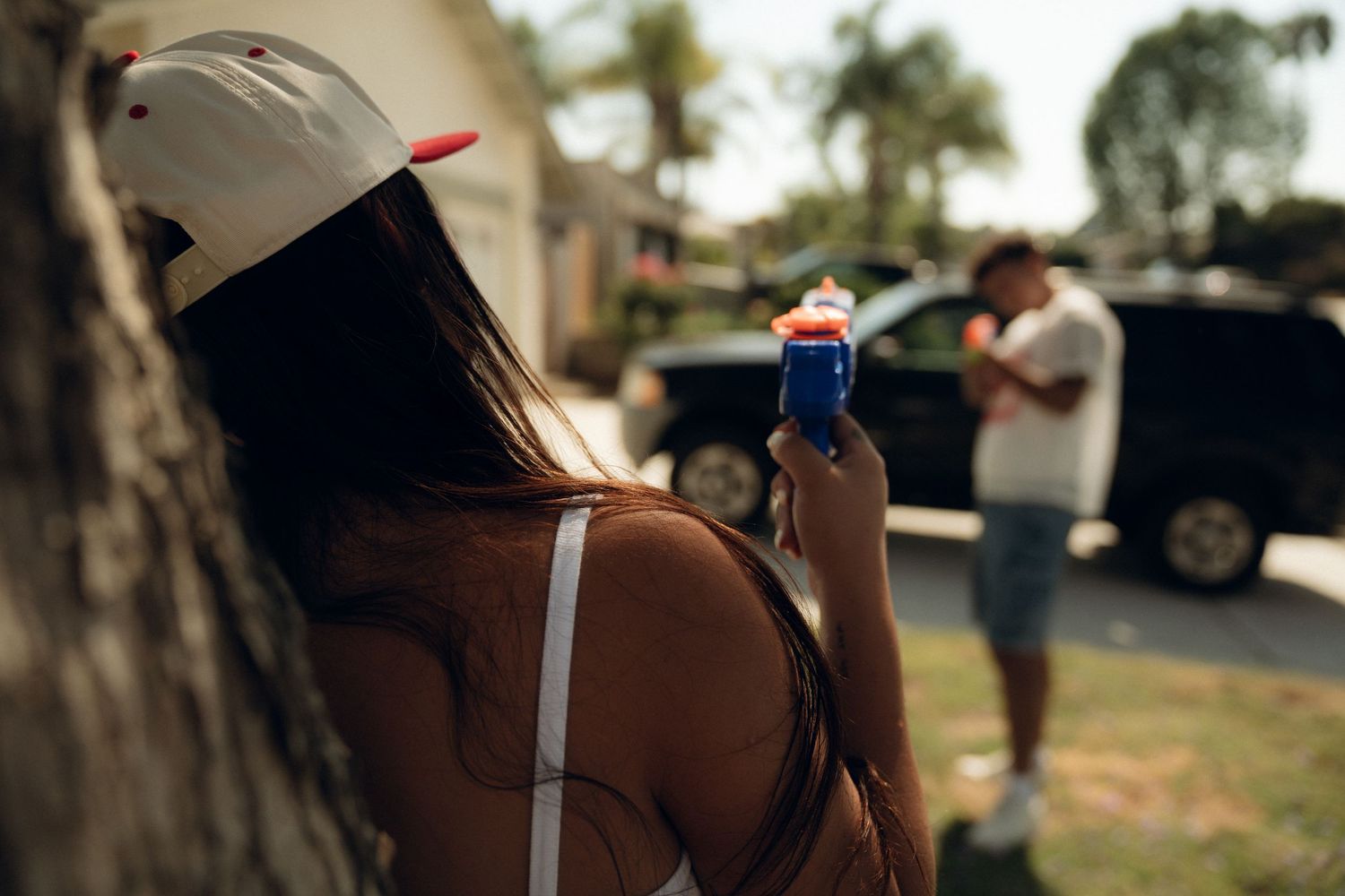 Someone in a white baseball cap and tank top holds a Pepsi can while standing outdoors in summer.